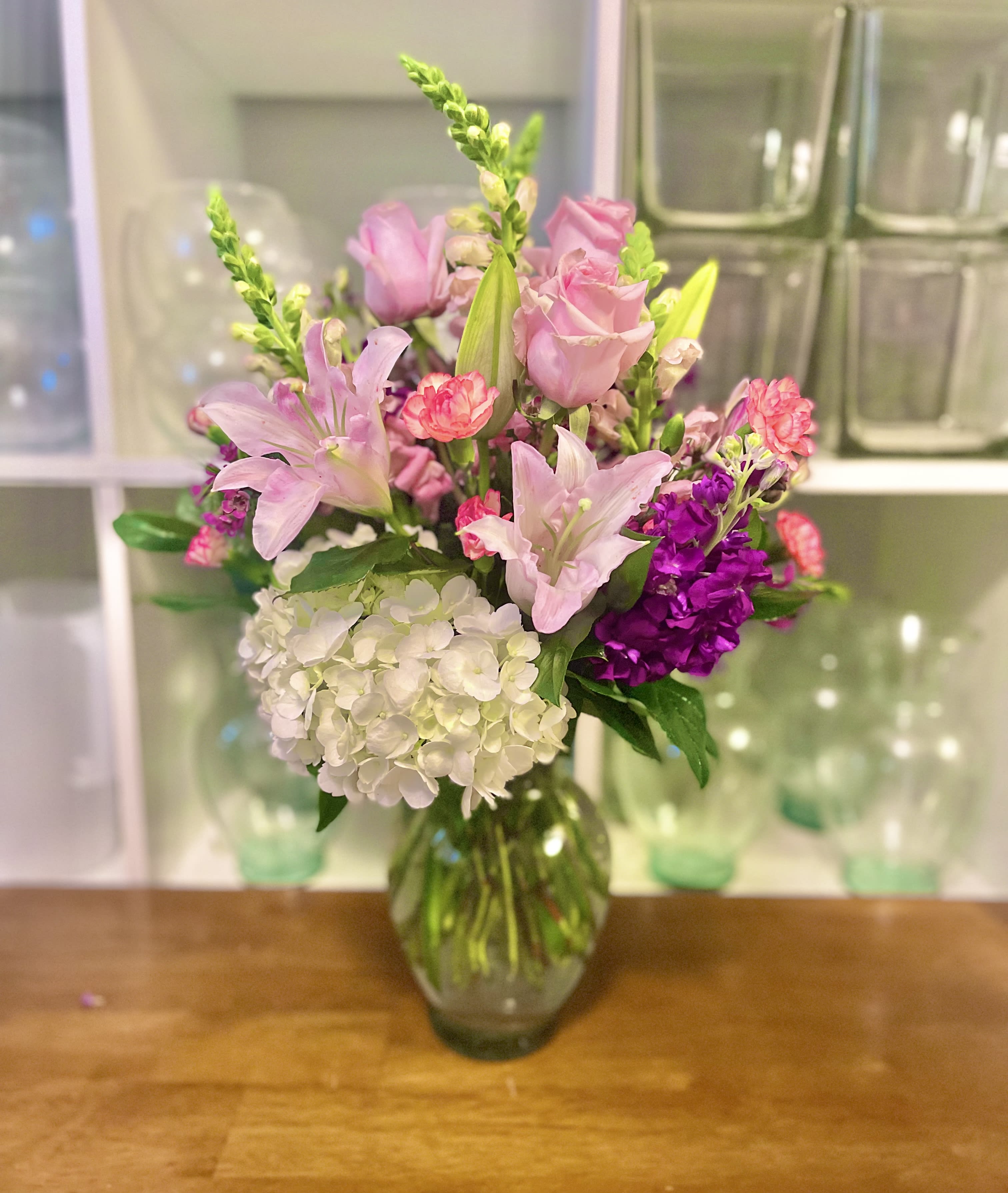 Lilly Rose Delight - Beautiful pink roses and lilies  with gorgeous snap dragon, stock mini carns and fluffy white hydrangea in a clear 8” vase.