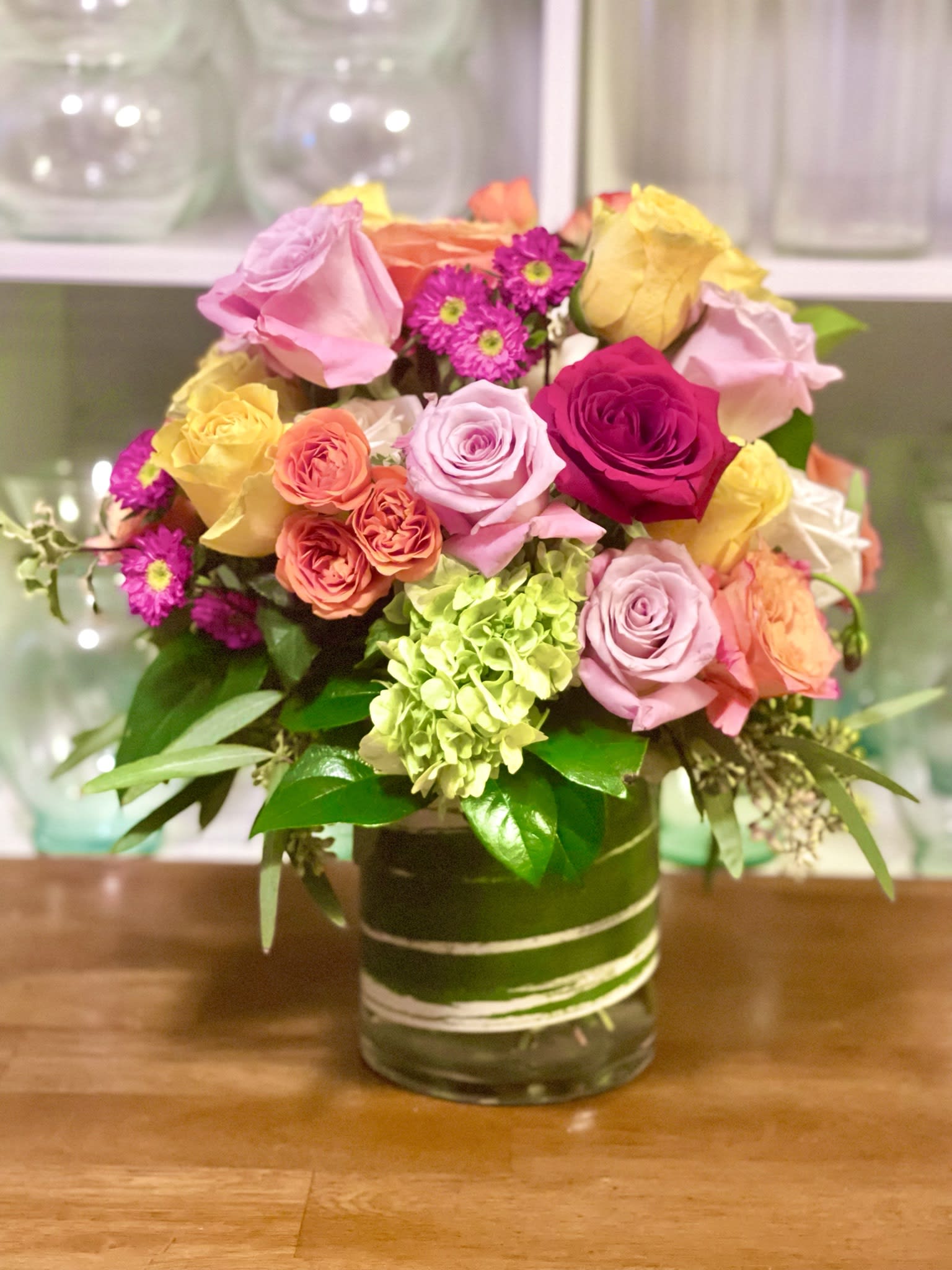 Mixed bouquet of pink, yellow, and orange roses in a glass vase