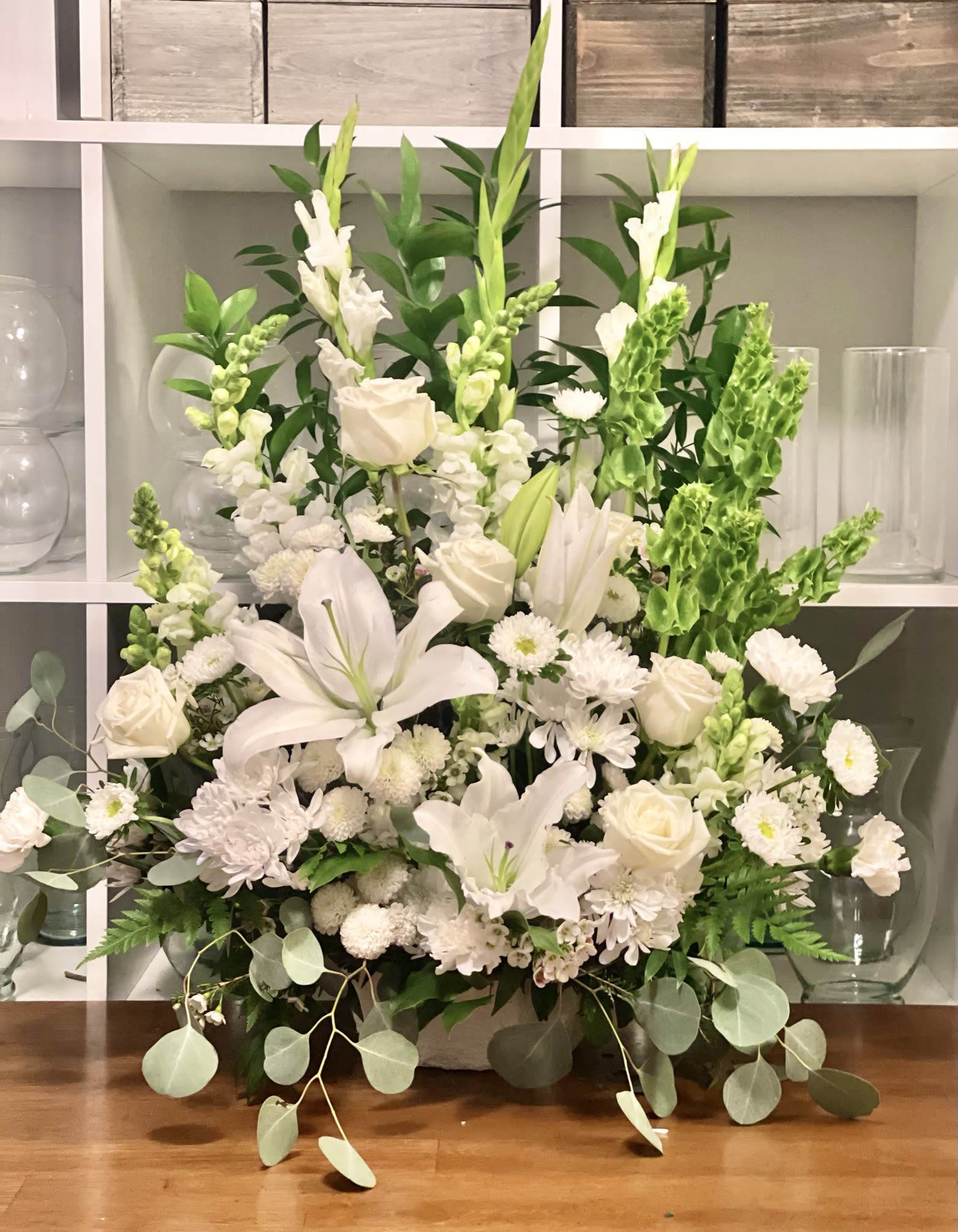 White floral arrangement with lilies, roses, and snapdragons in a low container