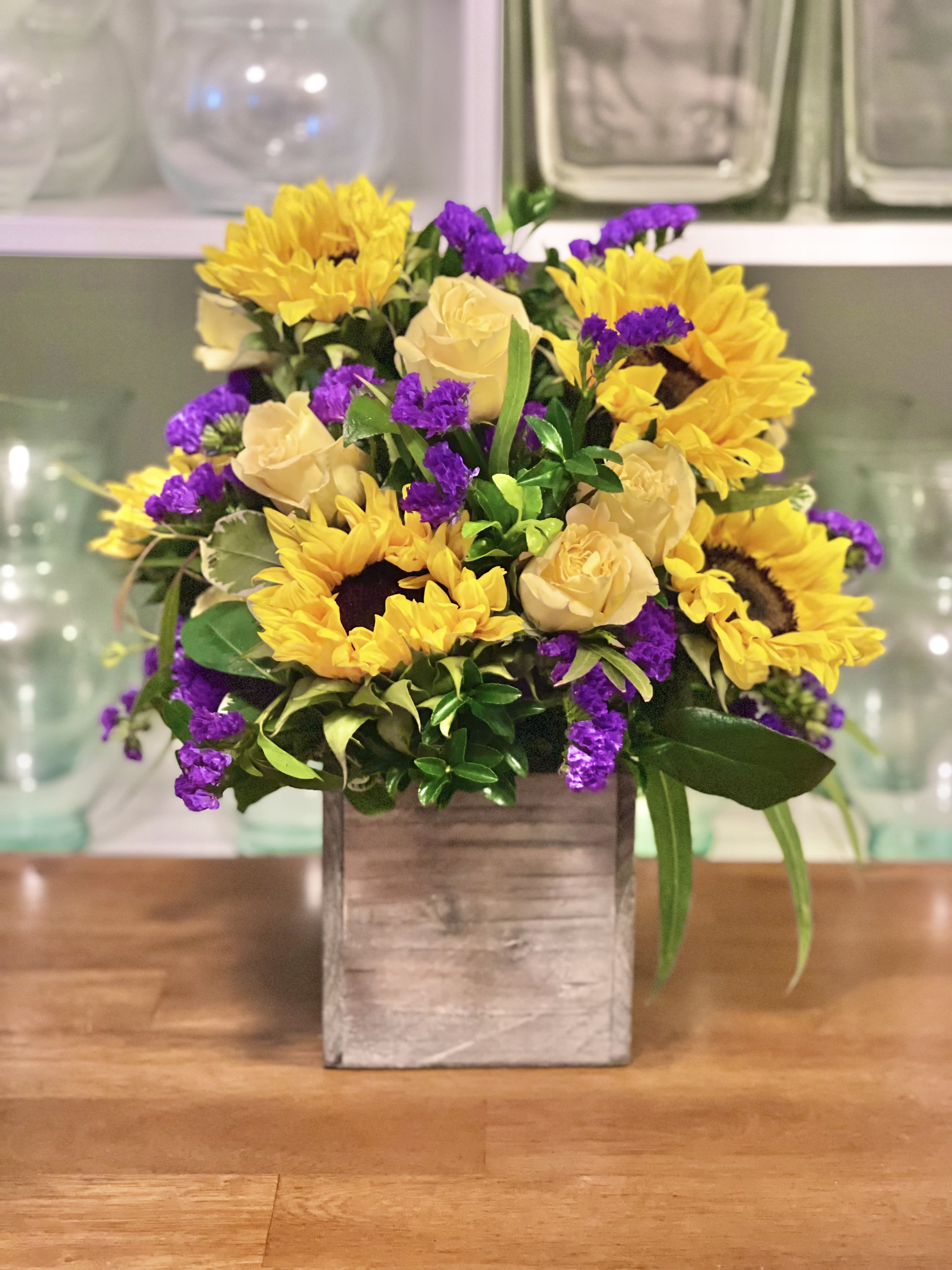 Yellow sunflowers, cream roses, and purple filler flowers in a wooden box