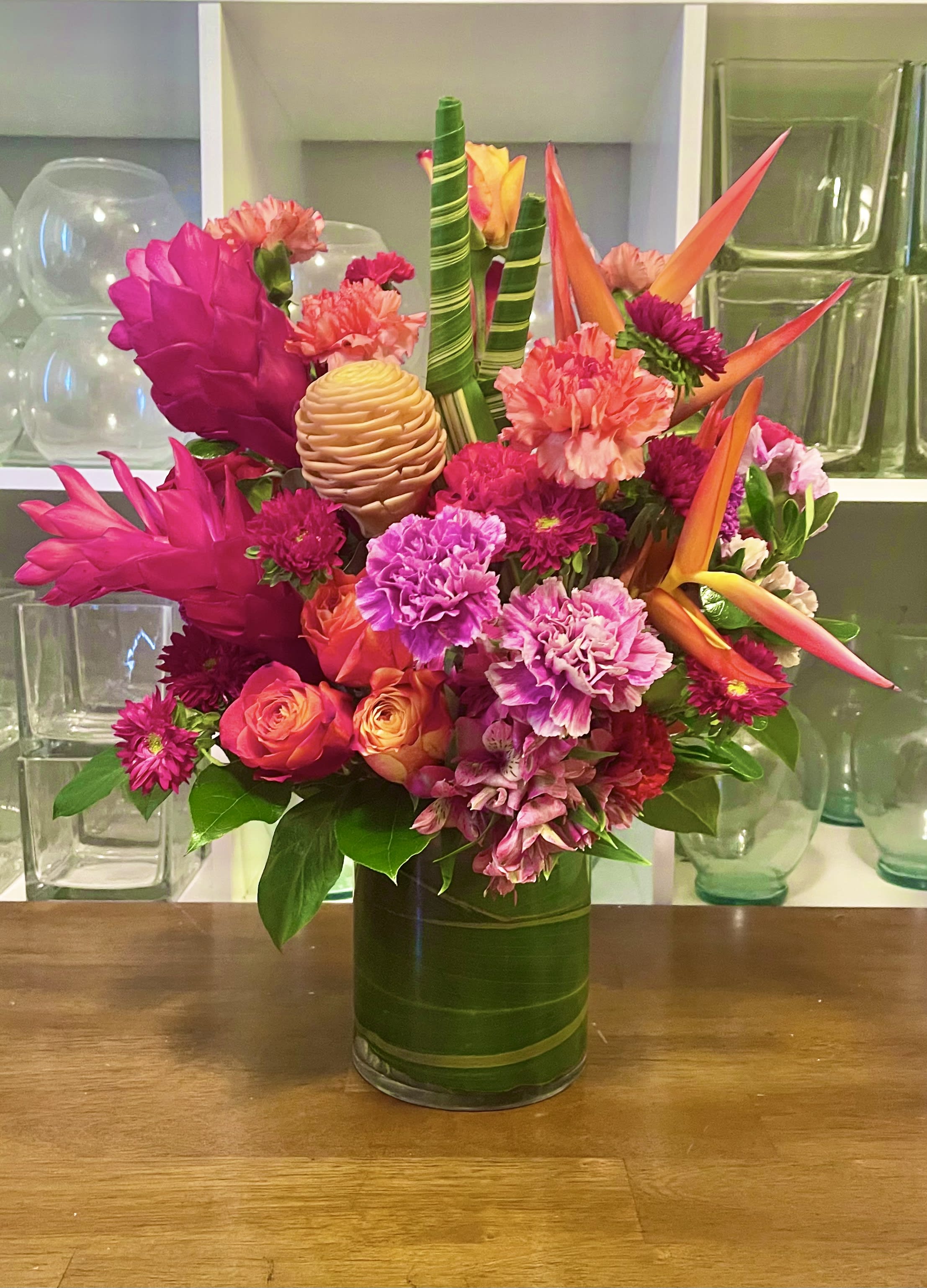 Ginger A Go Go - A beautiful warm arrangement filled with fresh cut roses, tropical flowers and long lasting carnations. In a 6” clear glass cylinder vase.