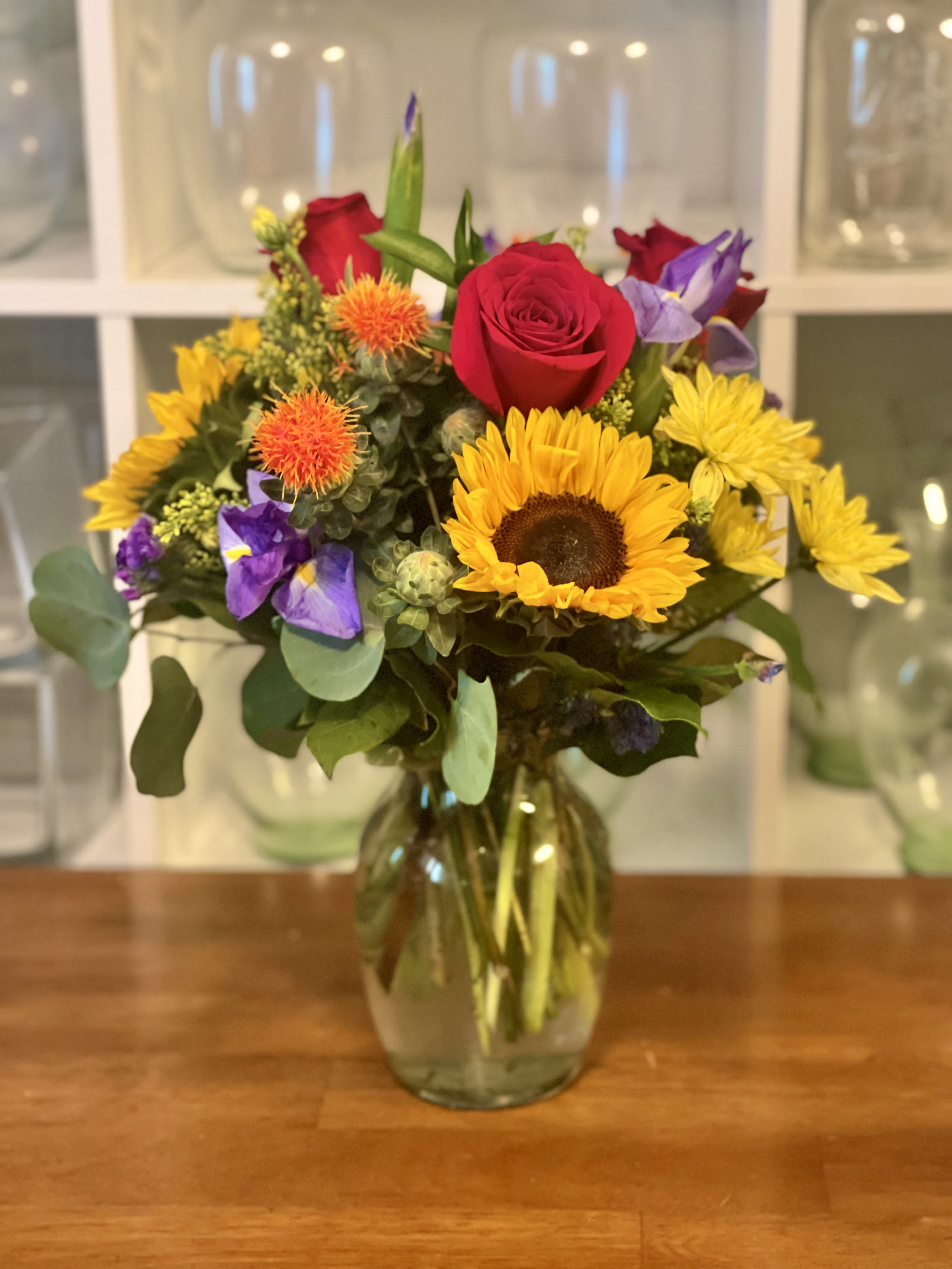 Mixed bouquet of sunflowers, red roses, and purple flowers in a glass vase
