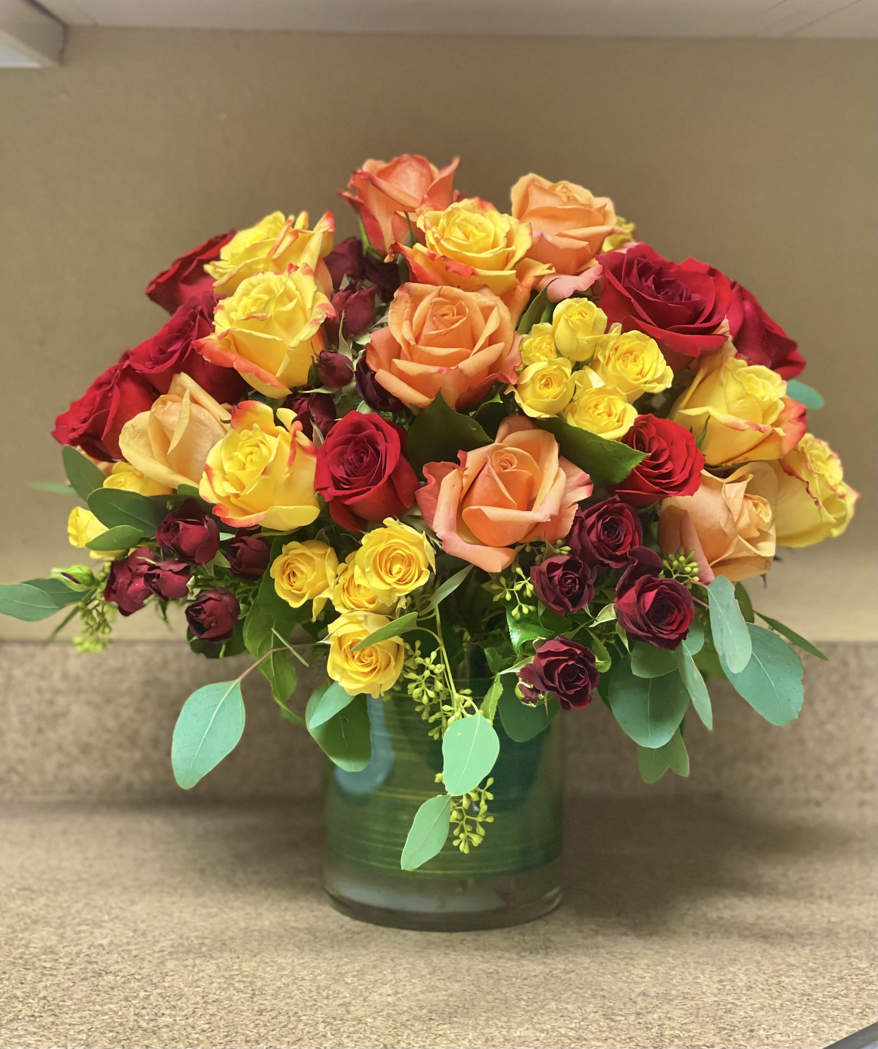 Mixed roses in red, yellow, and peach arranged in a glass vase
