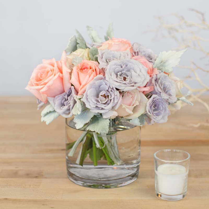 Pastel rose bouquet in a clear glass vase beside a white candle