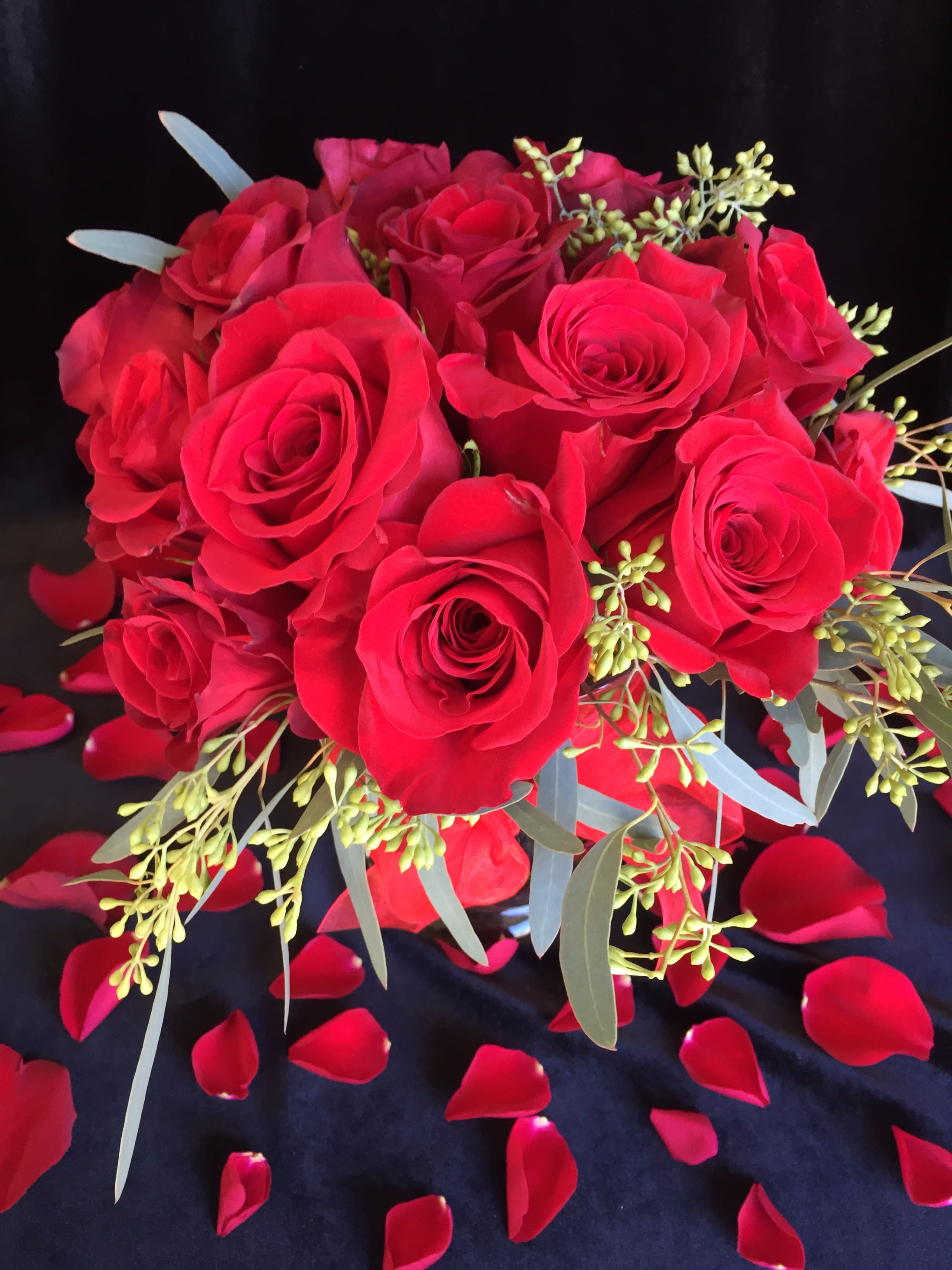 Bouquet of red roses with scattered rose petals on a dark background