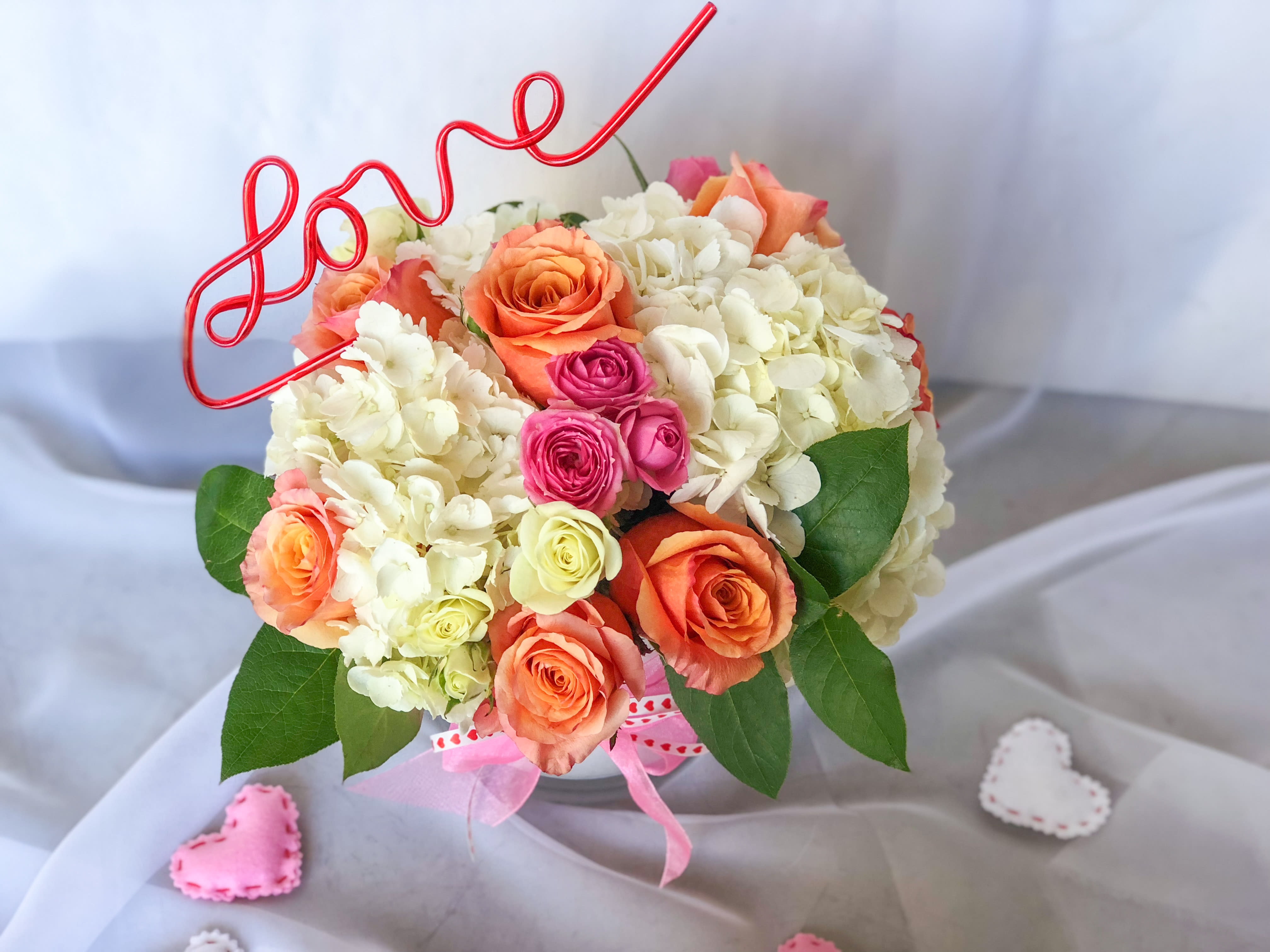 Bouquet of peach, pink, and white roses with a red wire "love" topper