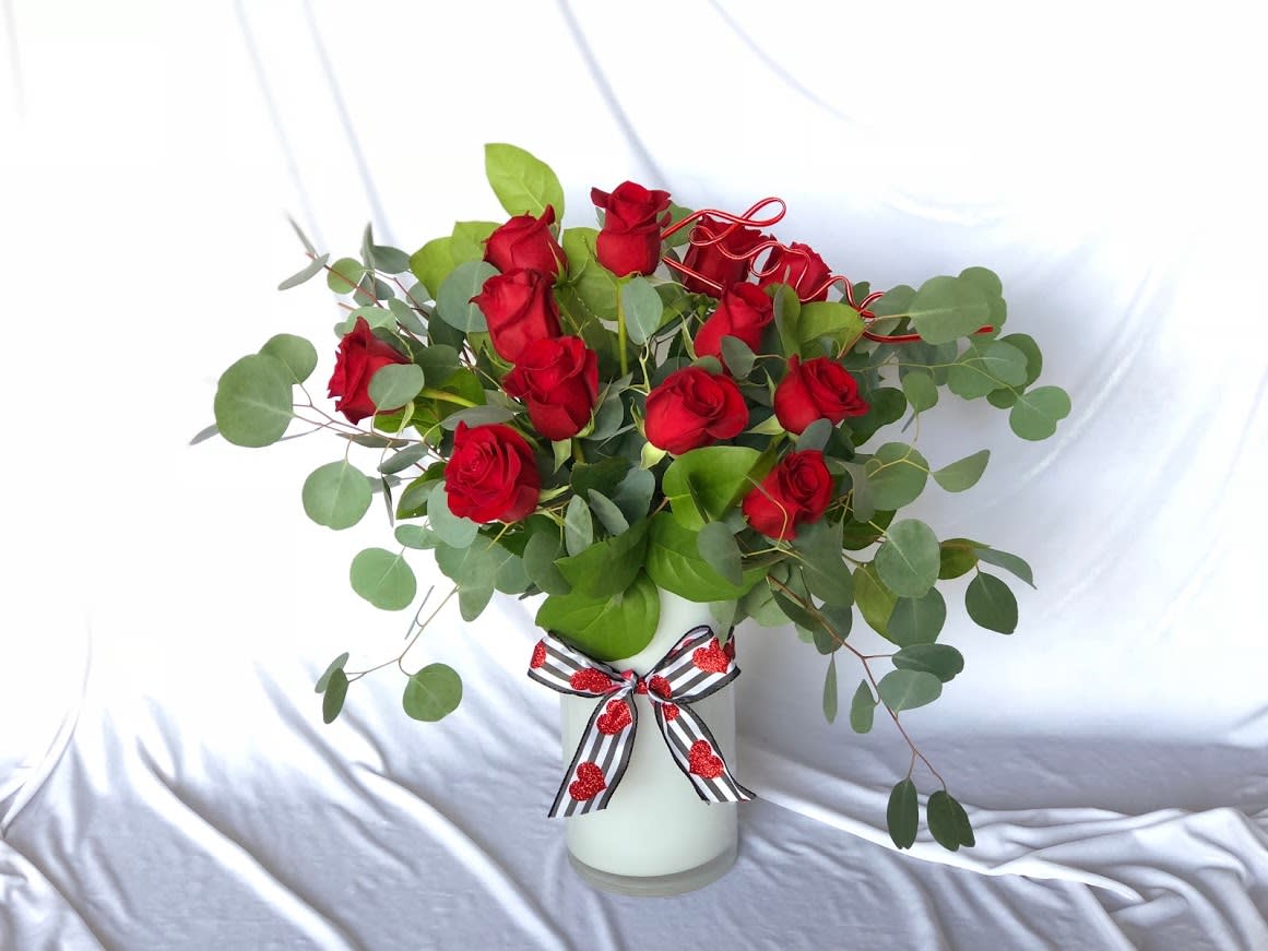 Red roses in a white vase with eucalyptus and a striped ribbon bow