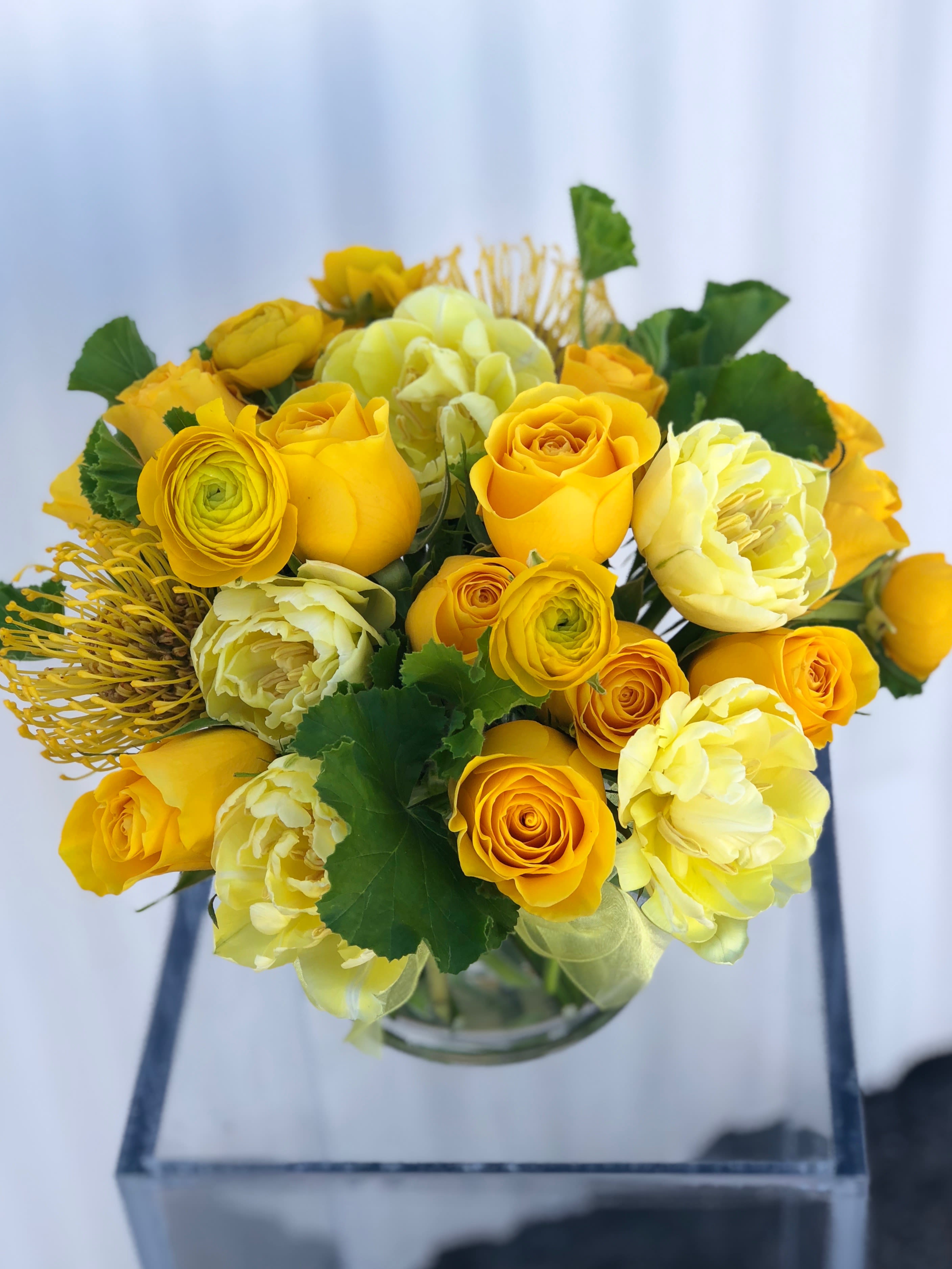 Yellow roses and pale blooms arranged in a clear glass vase