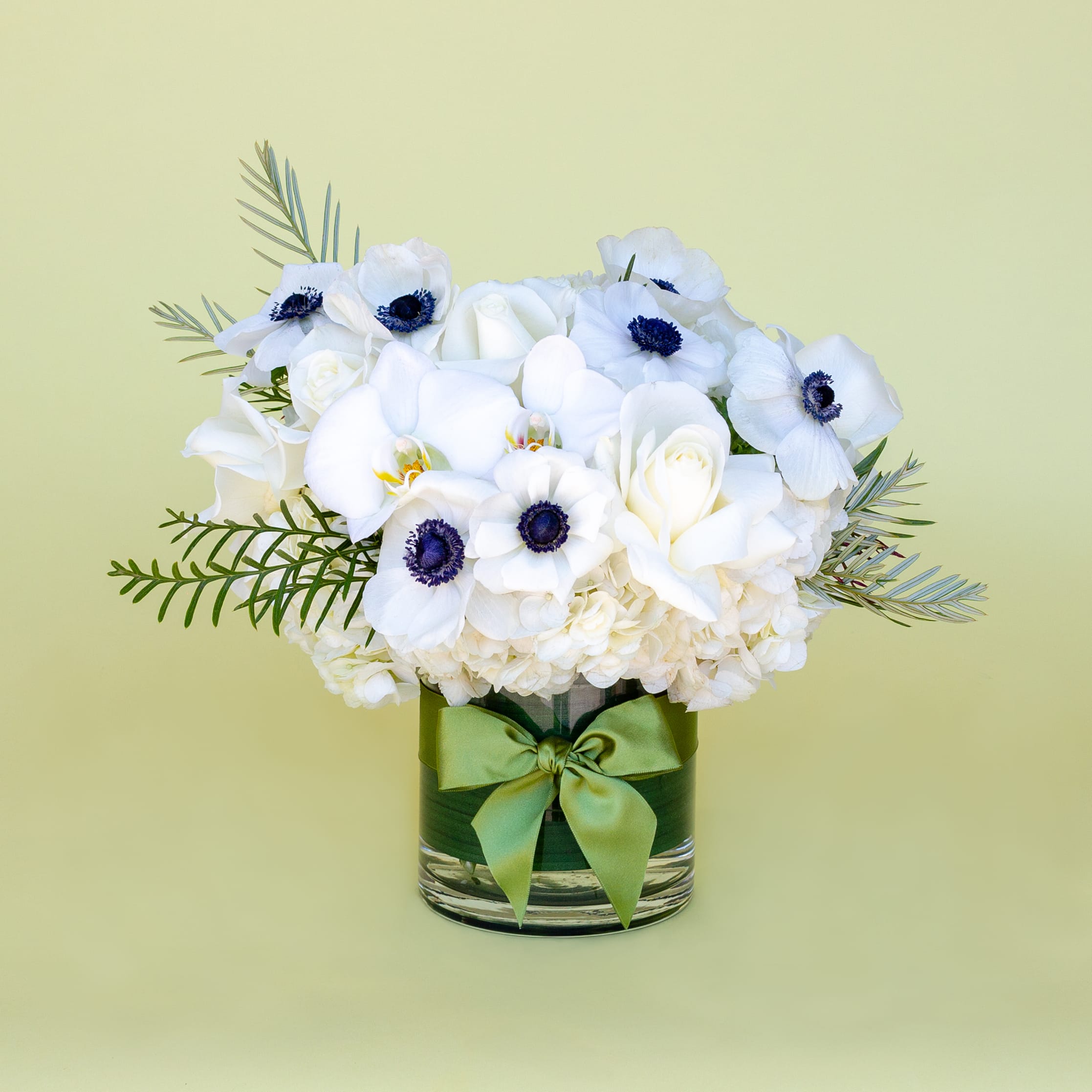 White floral arrangement in a glass vase with a green ribbon