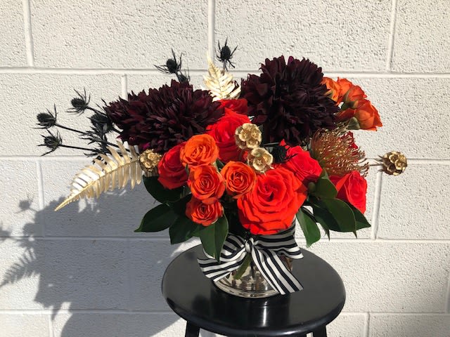 Red and orange rose arrangement in a silver vase with a striped ribbon