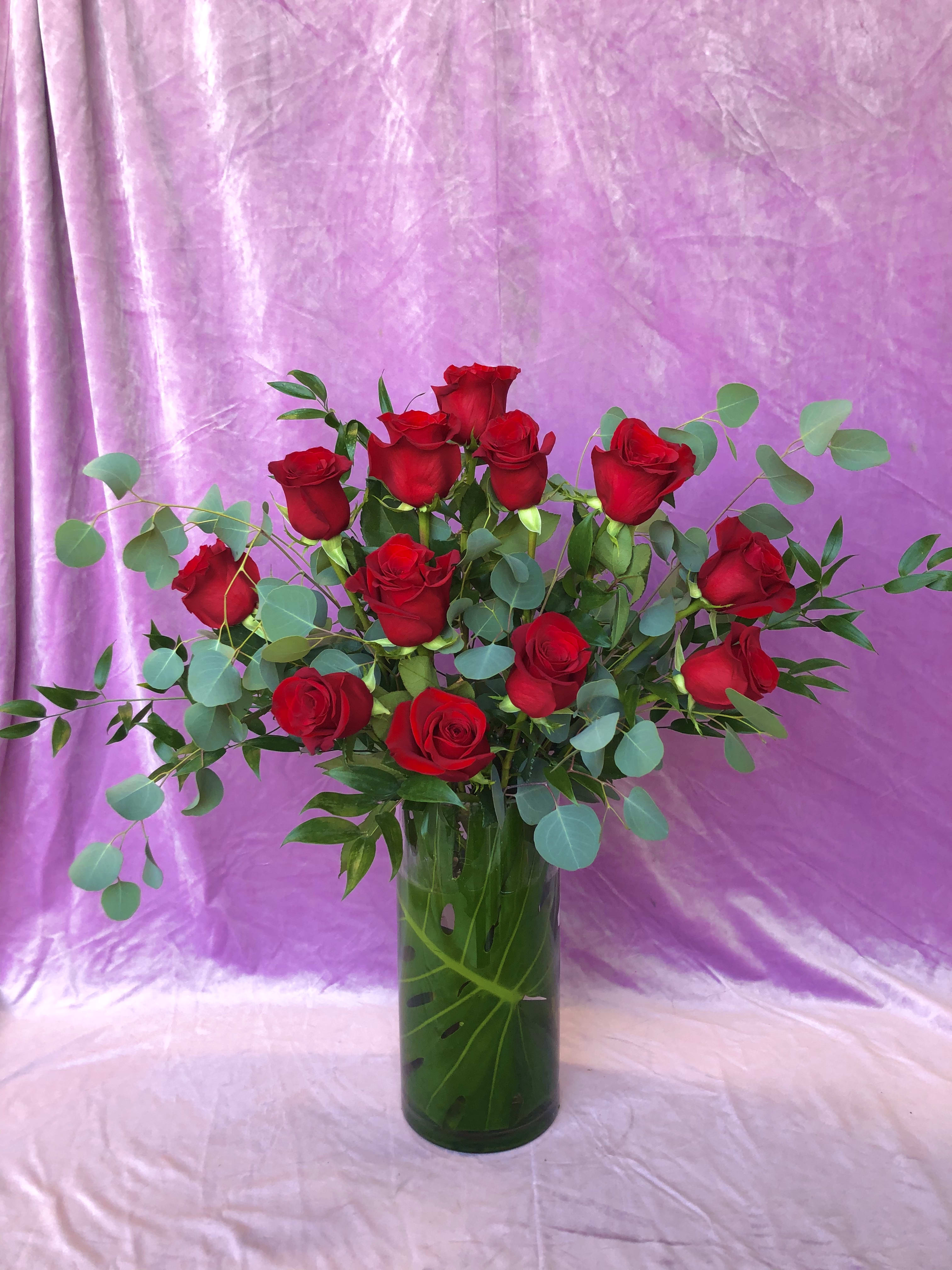 Red roses in a tall glass vase with eucalyptus foliage