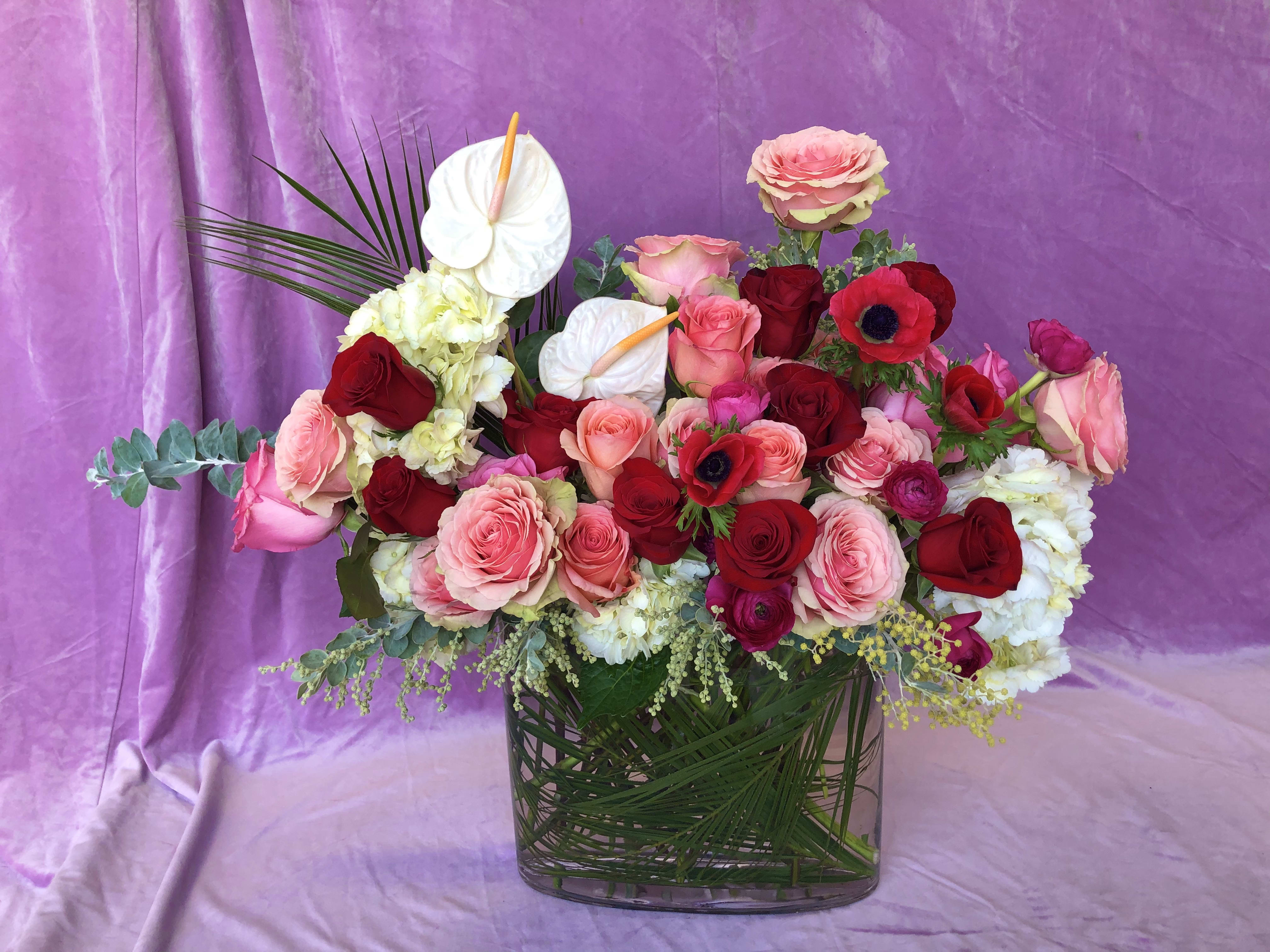 Mixed pink and red rose arrangement in a clear glass vase with white anthuriums