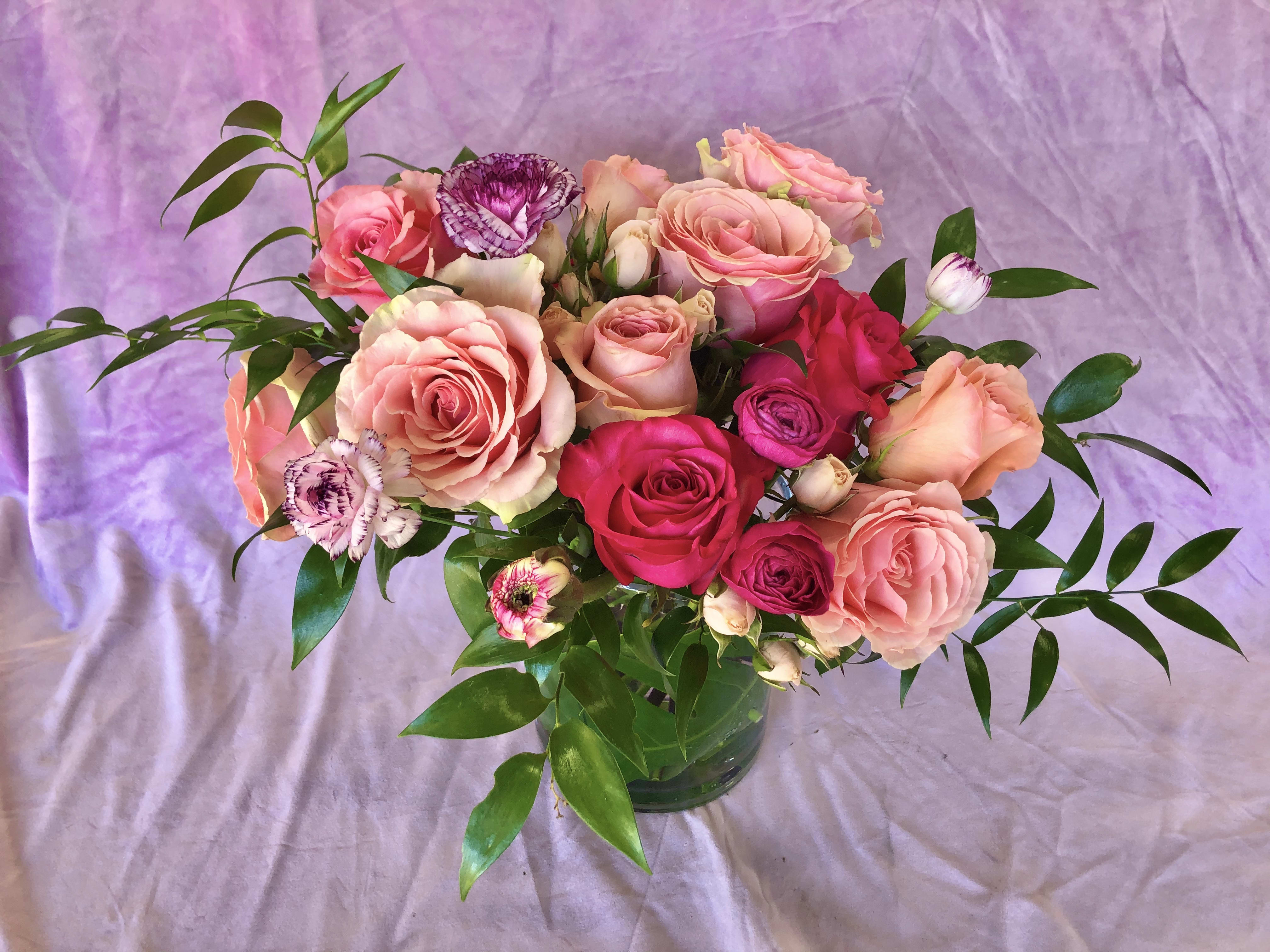 Pink and peach roses in a glass vase with purple flowers