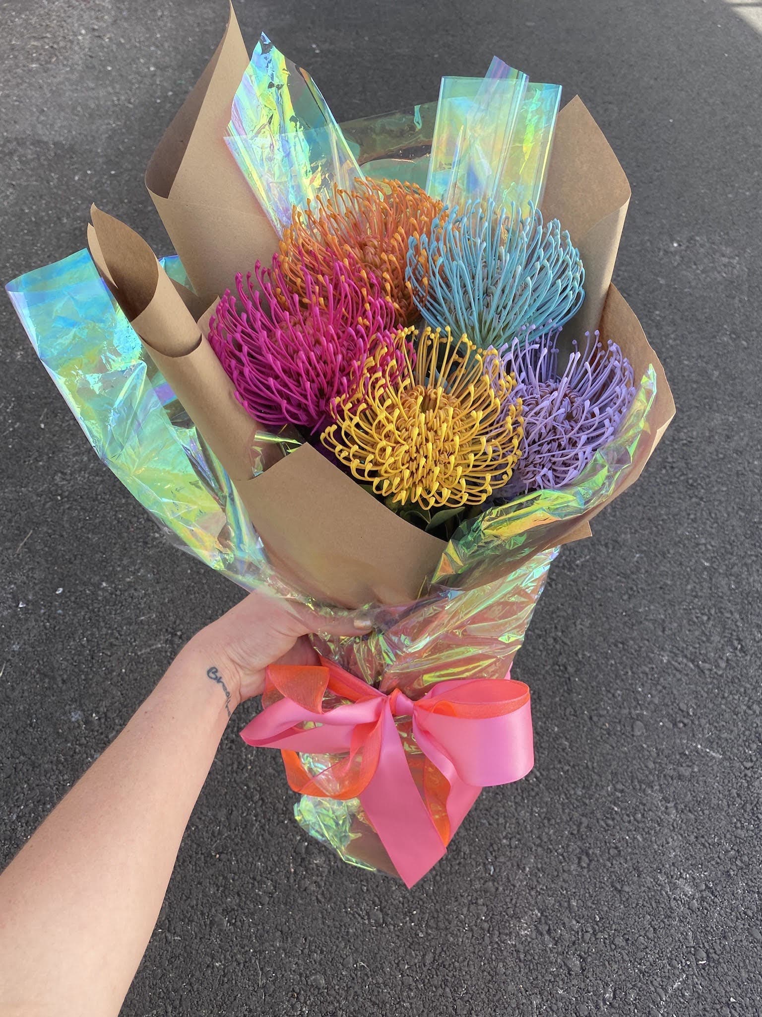 Bouquet of colorful pincushion protea wrapped in brown paper with a pink ribbon