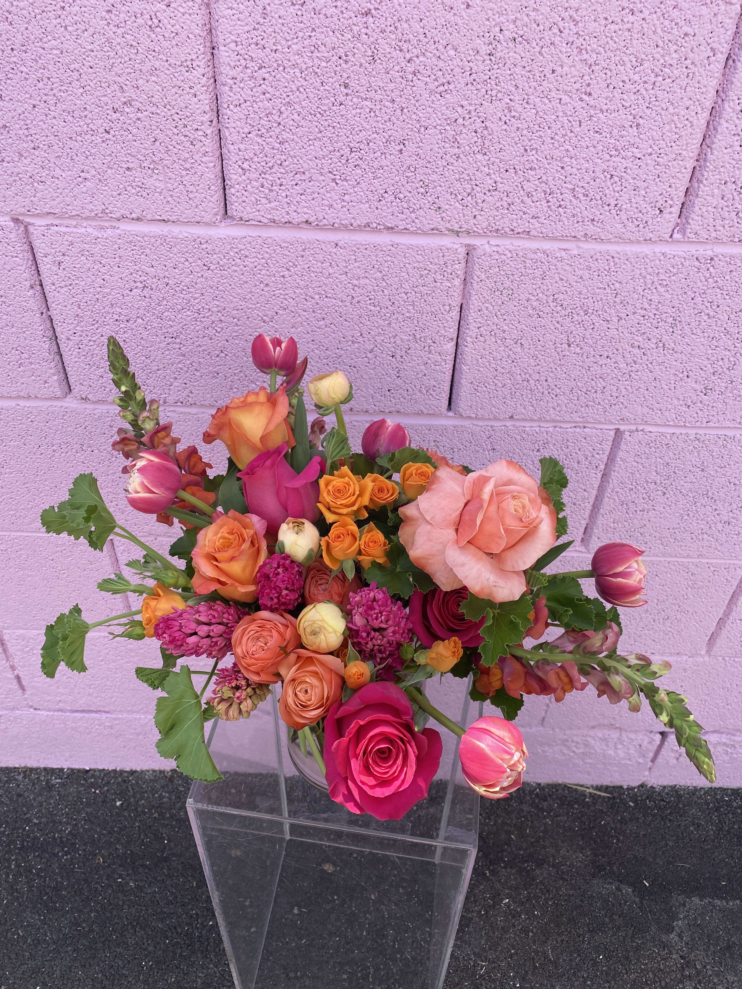 Mixed bouquet of pink, orange, and peach roses in a clear vase