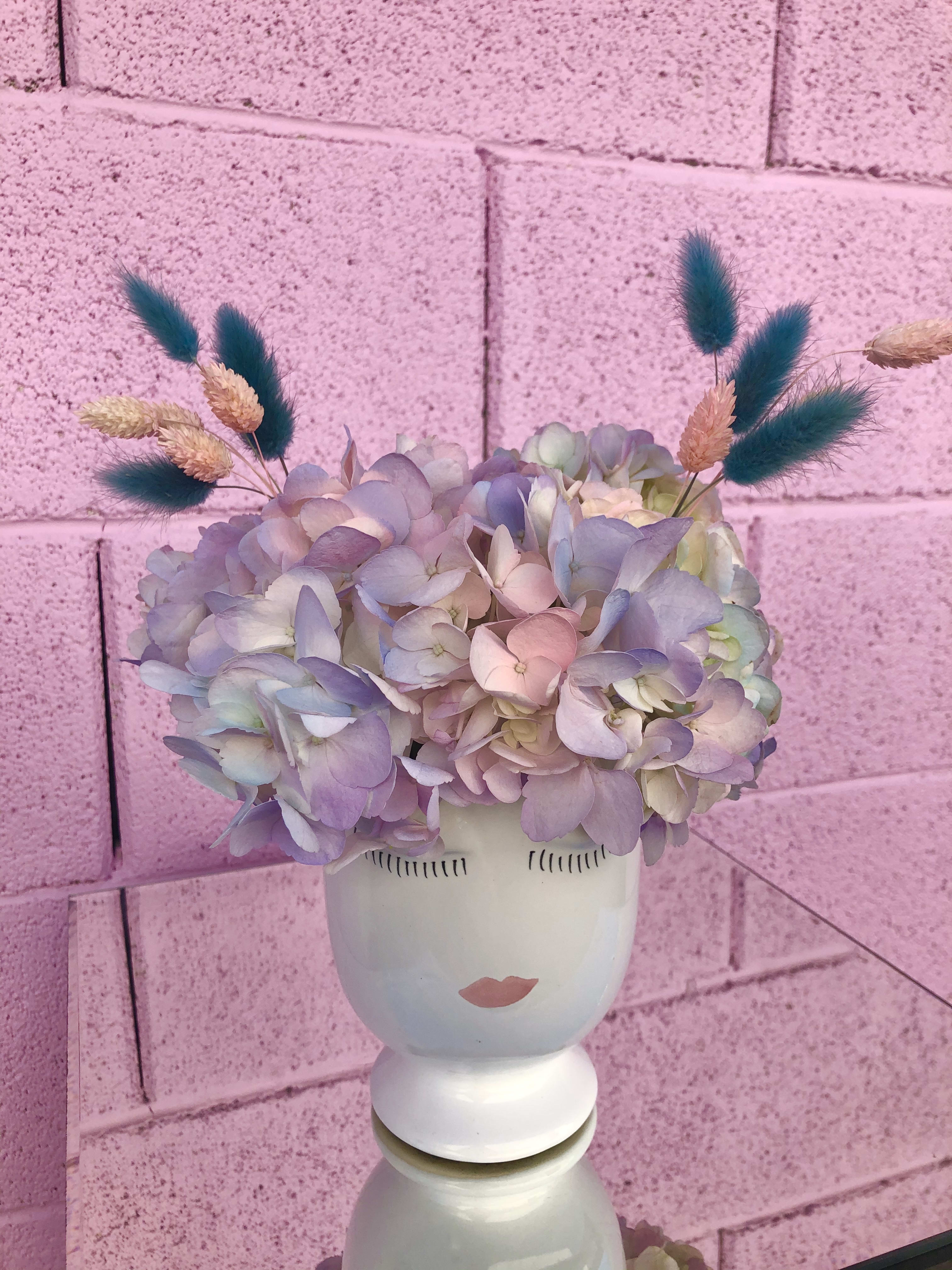 Pastel hydrangea arrangement in a white face vase with dried accents