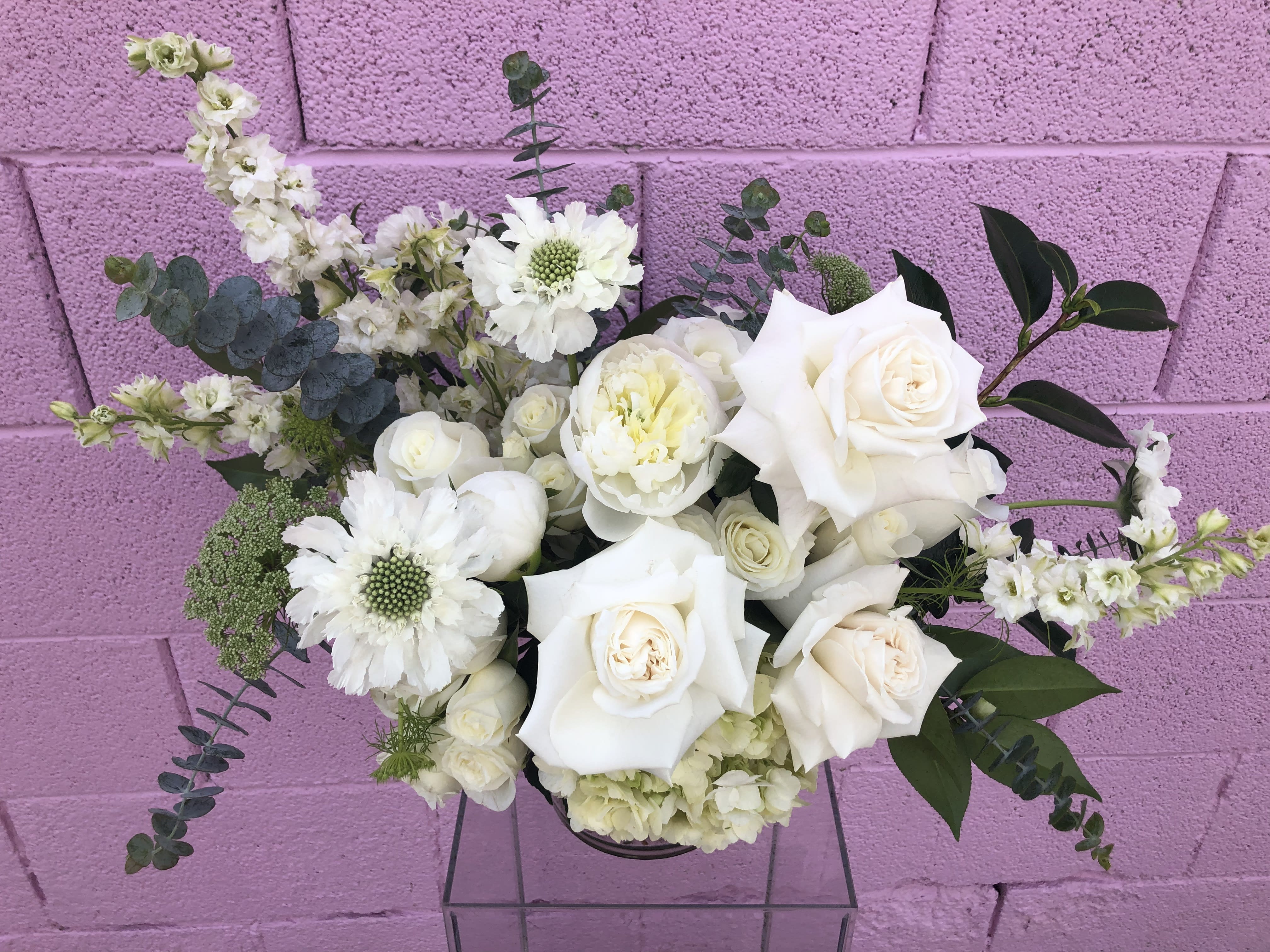White roses and mixed white flowers in a low arrangement against a pink wall