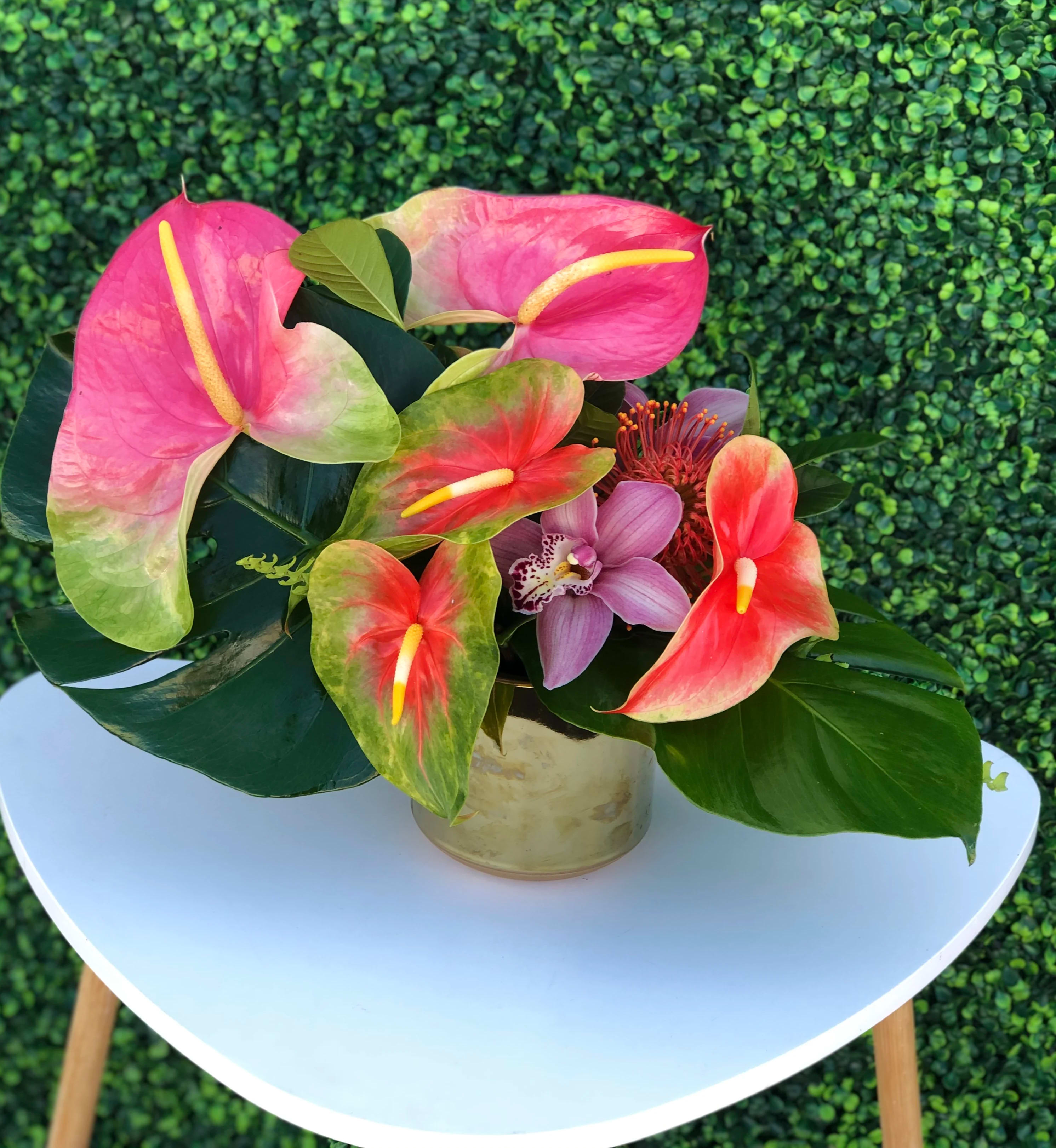 Pink and red anthuriums with a purple orchid in a gold vase
