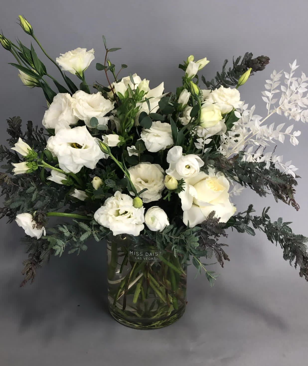 White floral arrangement in a glass vase with dark foliage