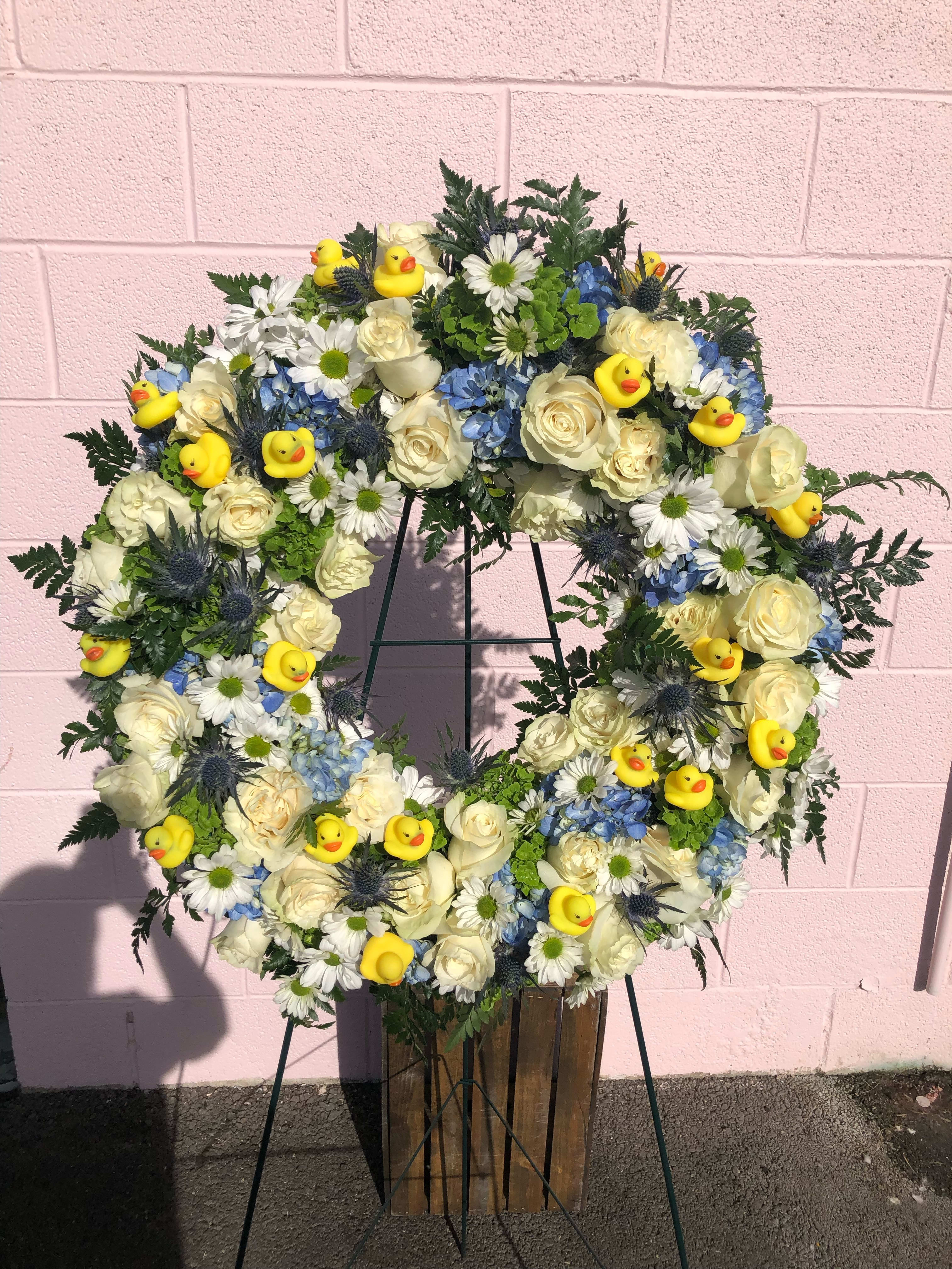 Wreath of white roses, blue flowers, and yellow duck decorations on a stand