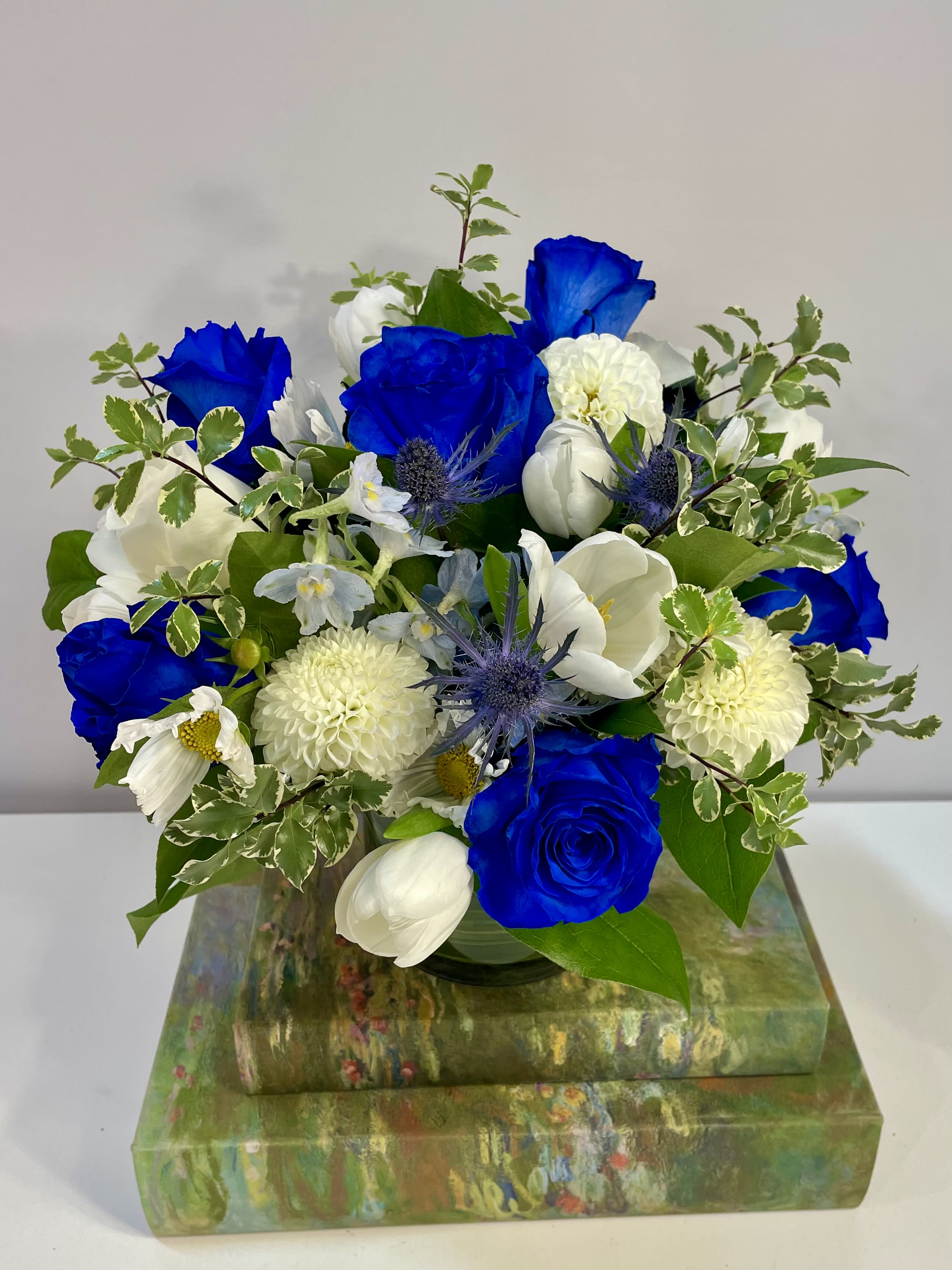 Blue and white flower arrangement in a glass vase on stacked decorative boxes