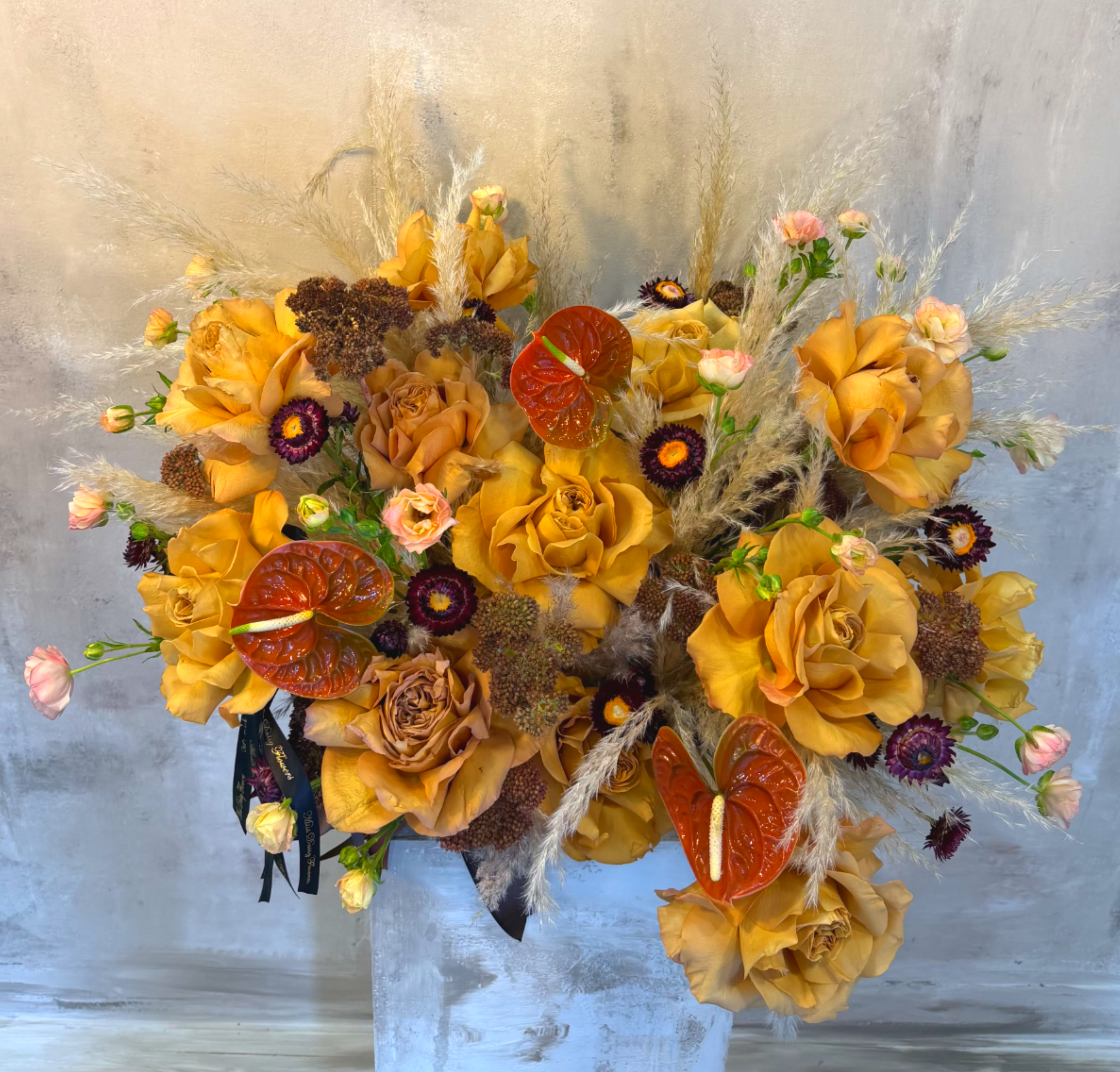 Toffee Garden - A rich and refined composition inspired by the warmth of autumn light and golden hues of nature. Toffee Garden blends velvety toffee and caramel-toned roses with glossy anthuriums, dried grasses, and soft textural blooms to create a lush, sculptural statement. Designed in our signature organic style, this arrangement evokes effortless sophistication — where modern design meets natural beauty.  Perfect for adding warmth to a space, celebrating an occasion, or gifting someone with truly elevated florals.