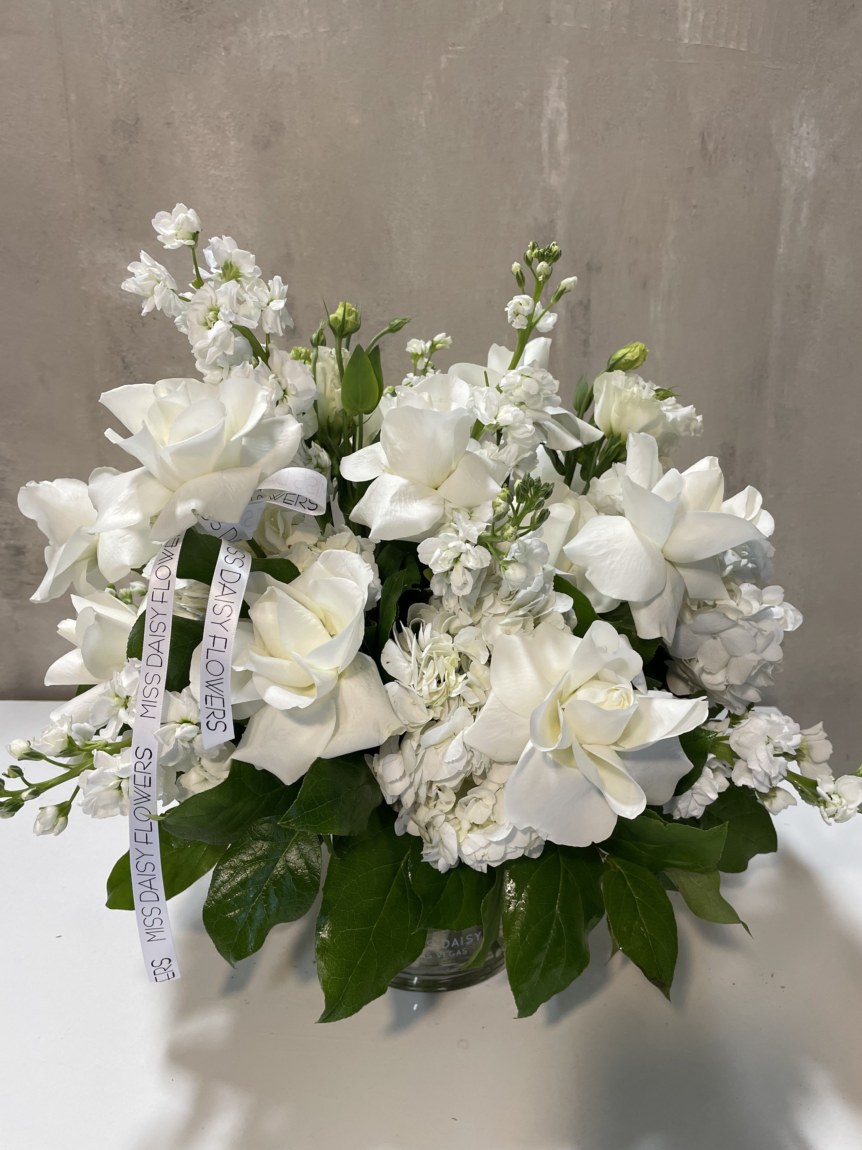 White floral arrangement in a glass vase with ribbon streamers