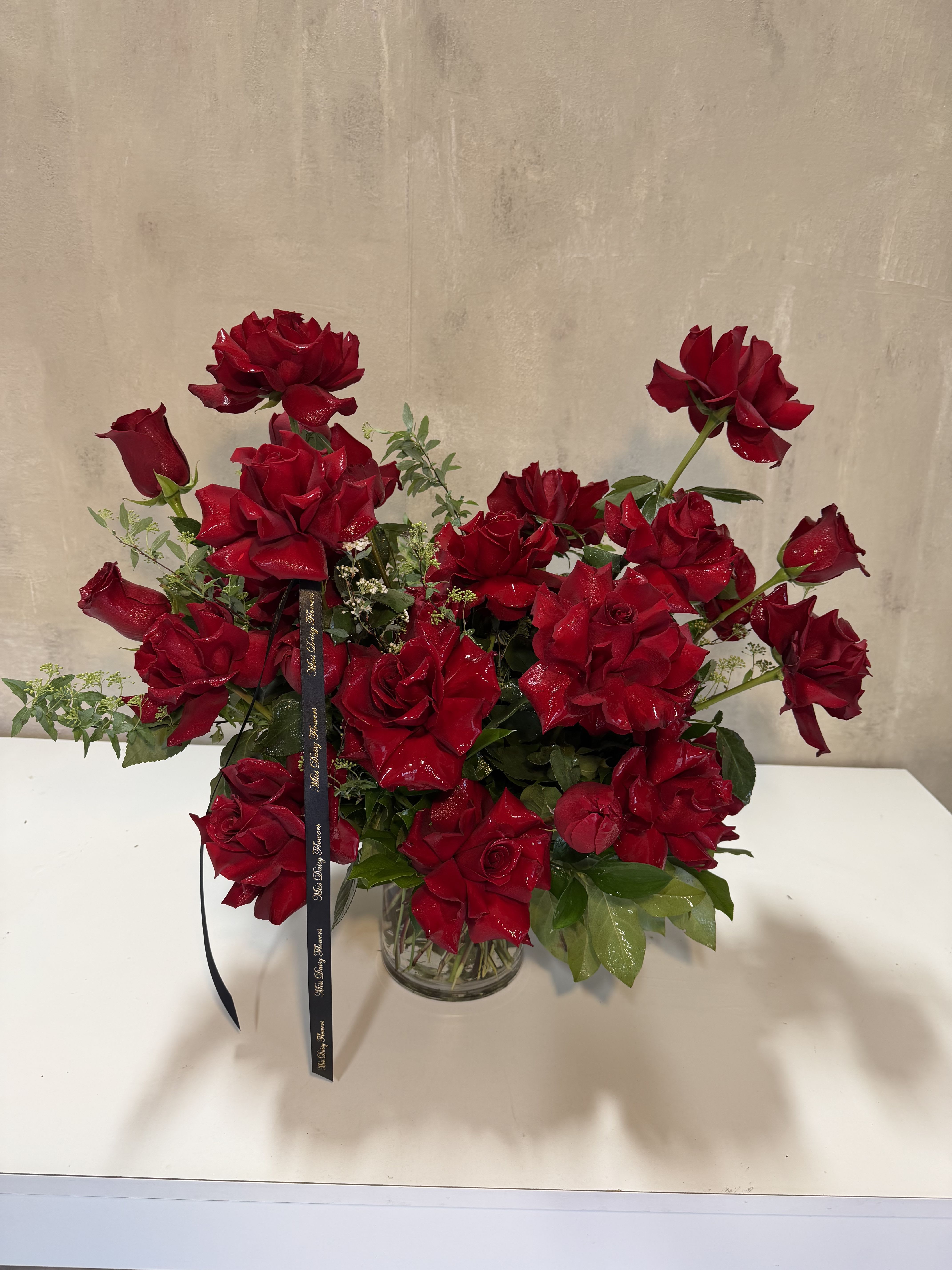 Red roses arranged in a clear glass vase with a black ribbon