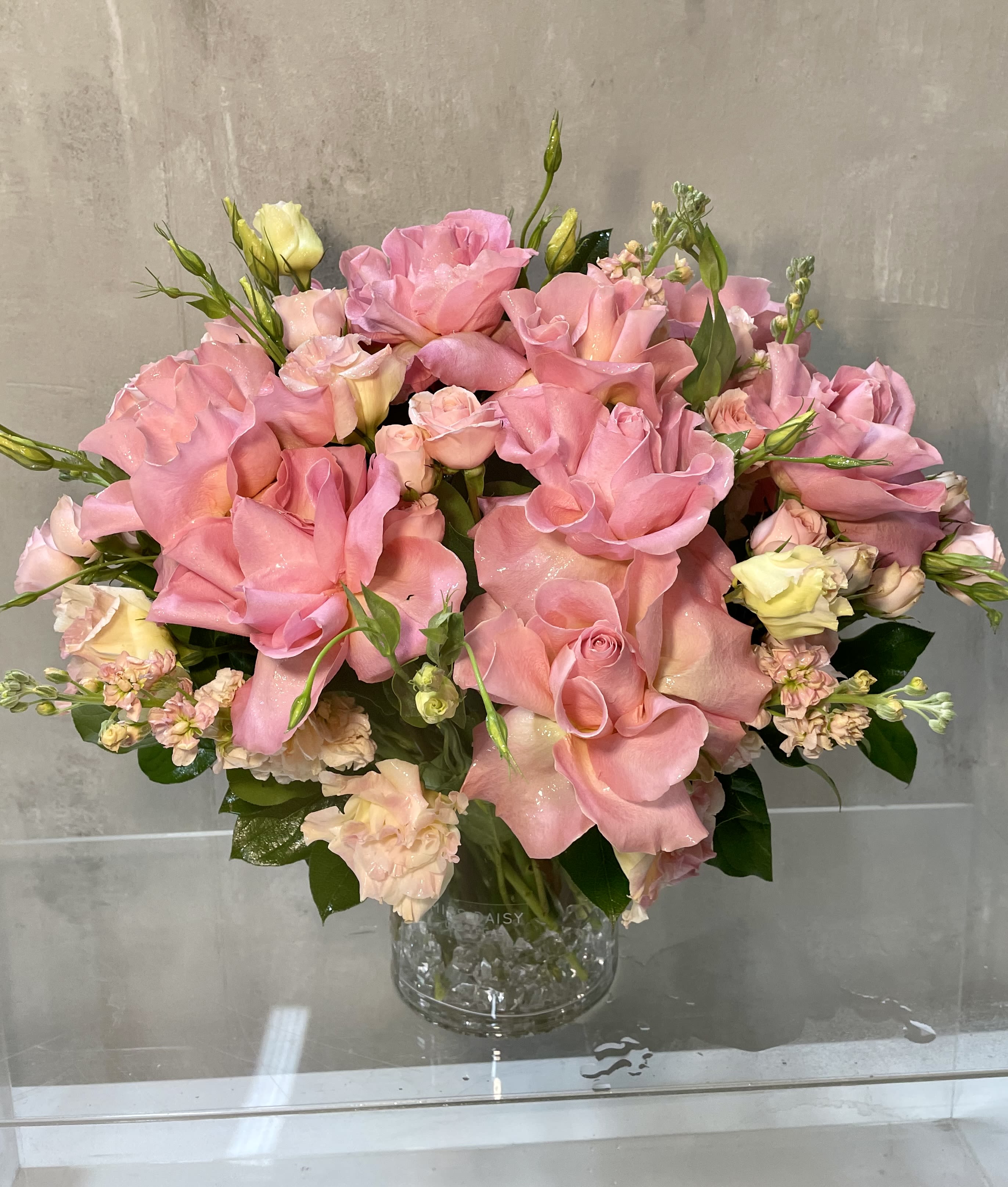 Pink roses and pale spray flowers arranged in a clear glass vase.