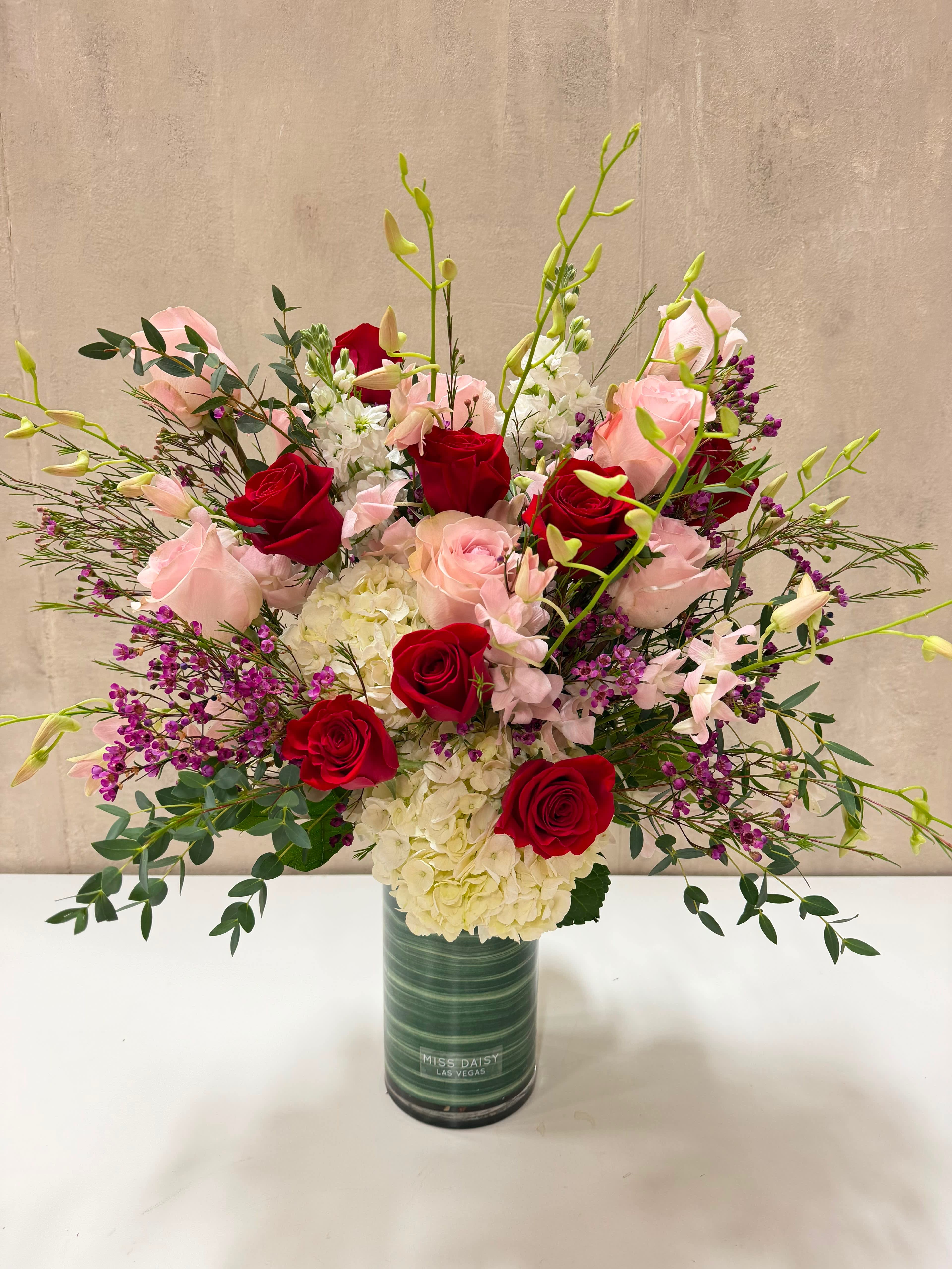 Red and blush roses in a tall green vase with white hydrangeas