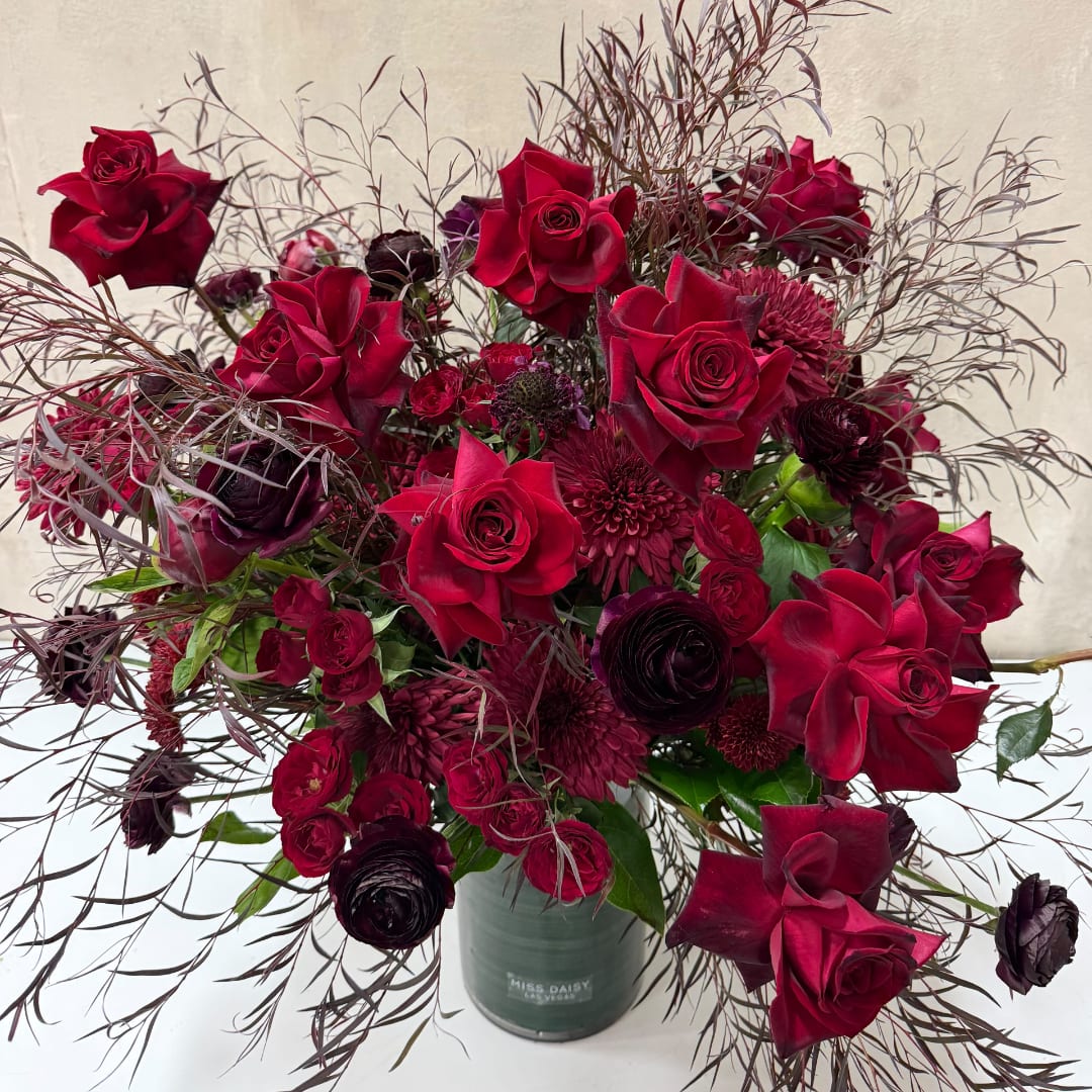 Deep red roses and burgundy blooms in a green vase