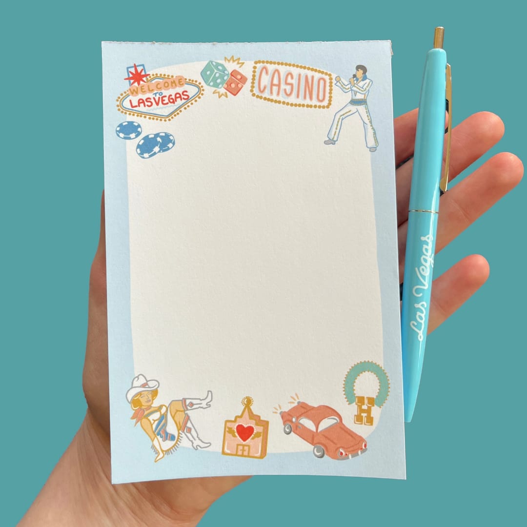 Las Vegas-themed notepad held with a turquoise pen clipped to the side