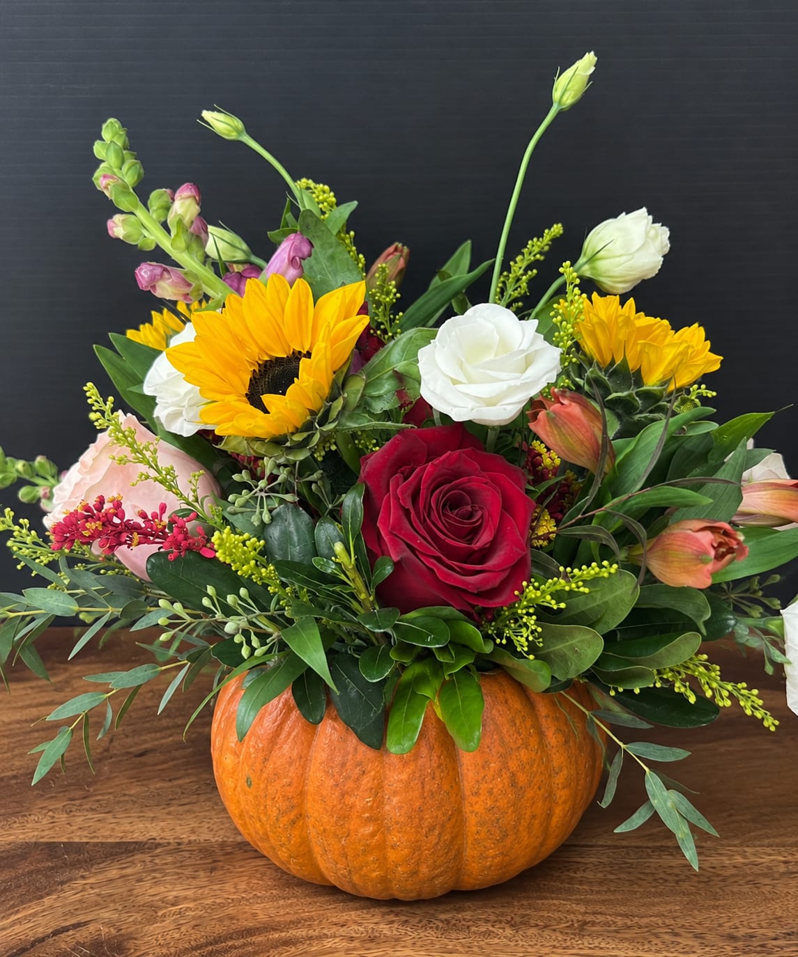 Floral arrangement in a pumpkin container with roses, sunflowers, and mixed blooms