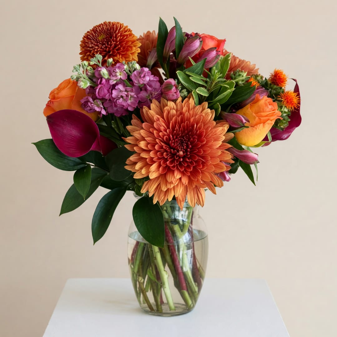 Colorful mixed bouquet in a clear glass vase with orange and purple blooms