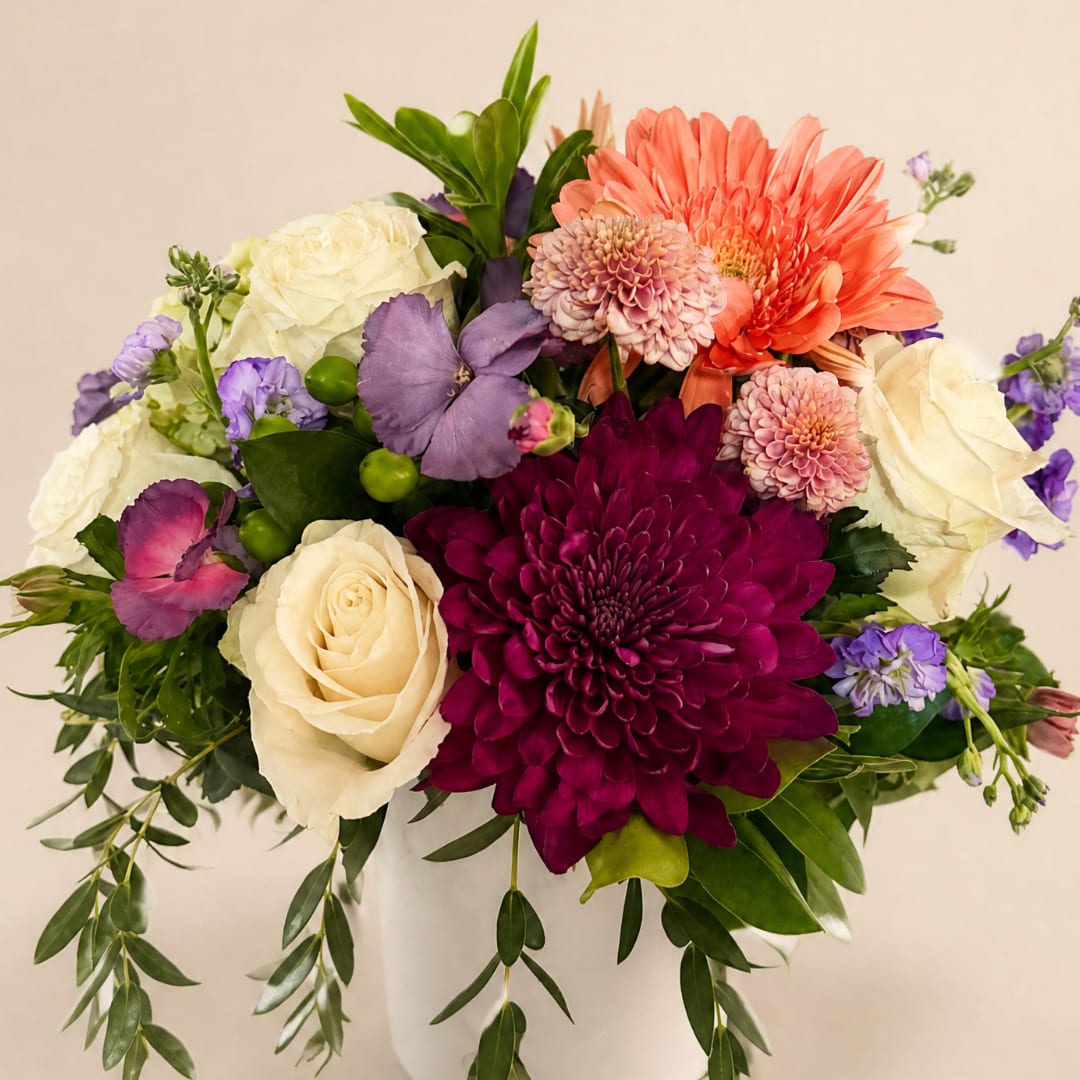 Mixed bouquet of roses, chrysanthemums, and purple flowers in a white vase
