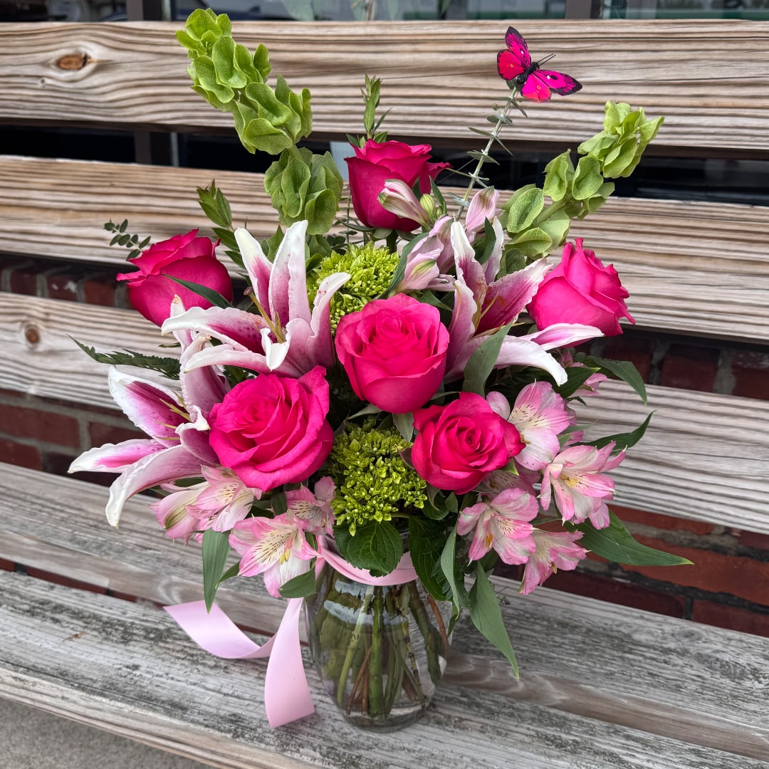 Pink roses and lilies arranged in a glass vase with a ribbon.