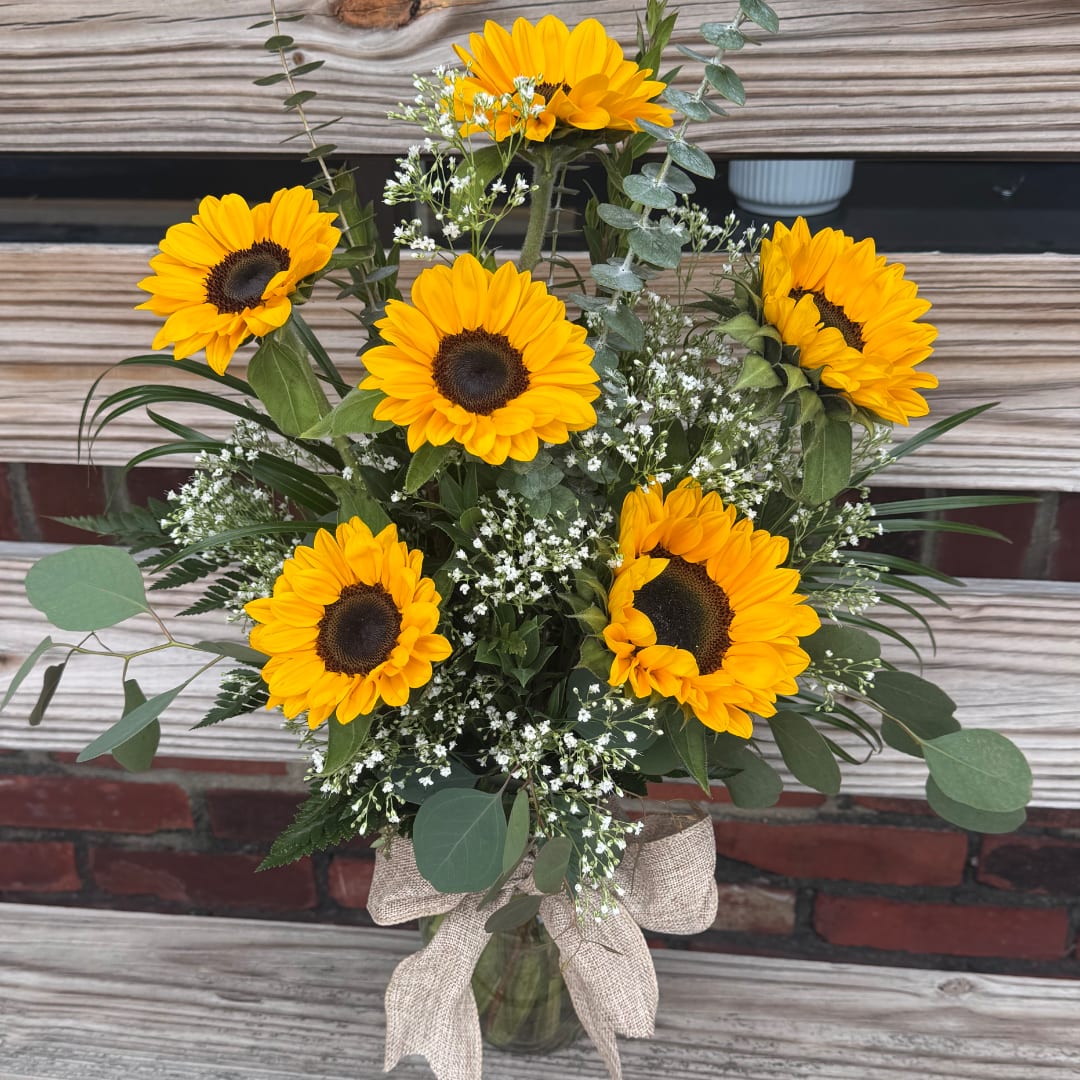 Bouquet of yellow sunflowers in a glass vase with a burlap bow
