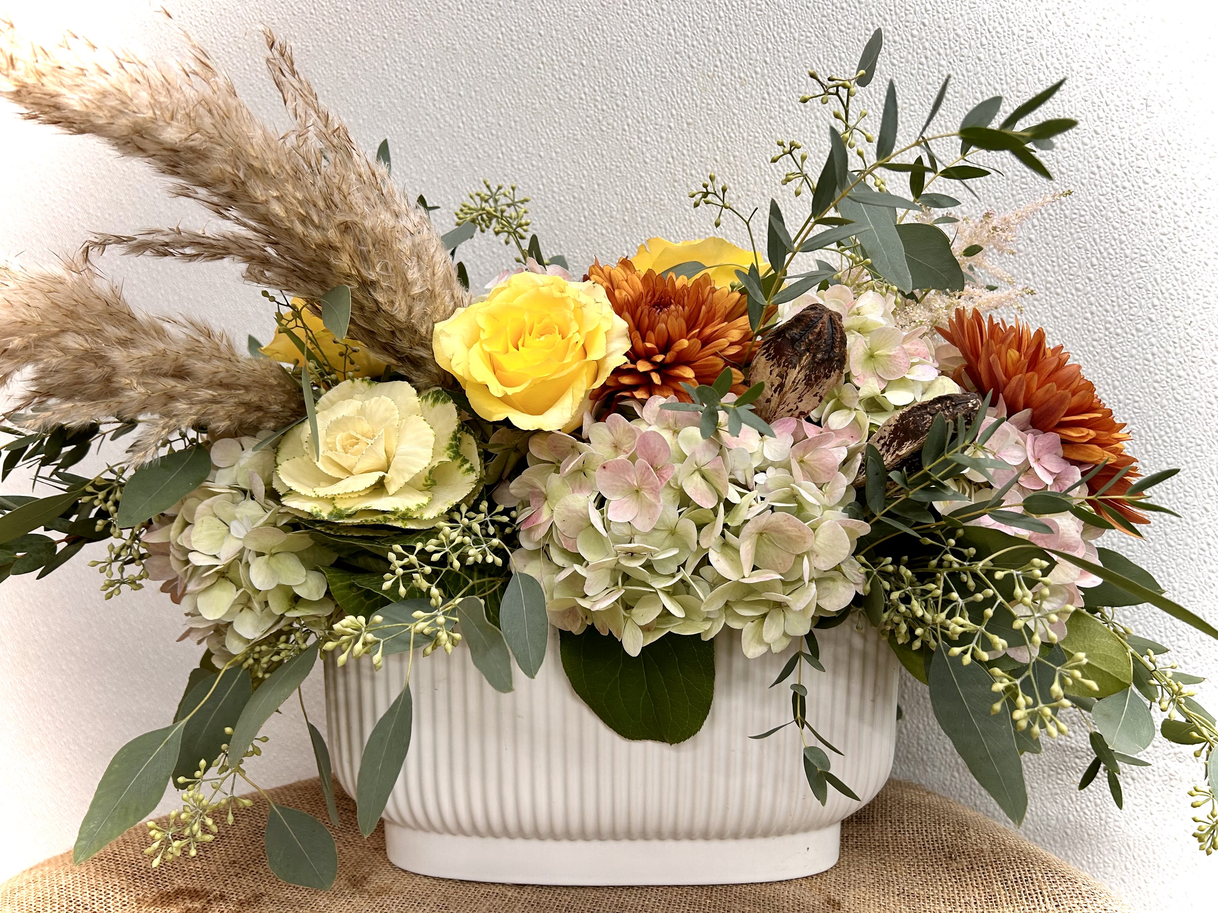 Mixed floral arrangement in a white ribbed container with yellow and orange blooms