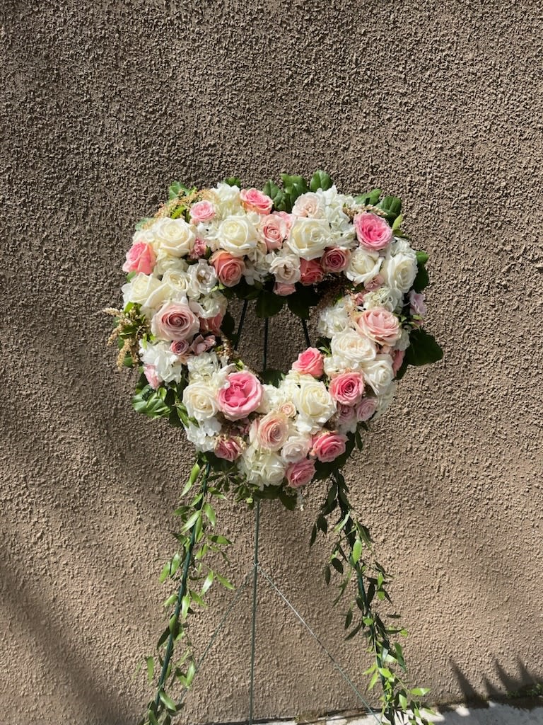 Heart-shaped floral wreath of pink and white roses on a stand