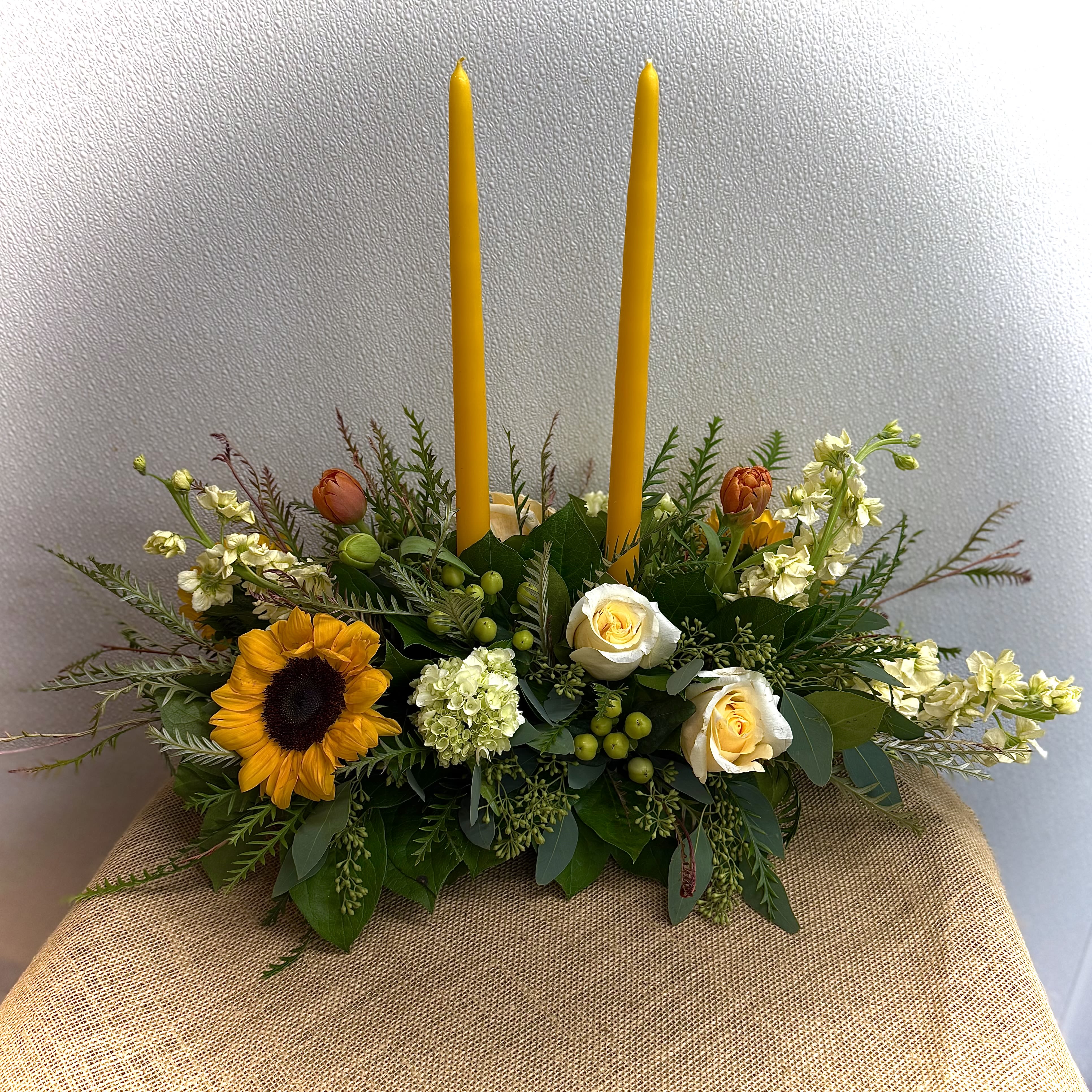 Floral centerpiece with two tall yellow candles and sunflowers in a low arrangement