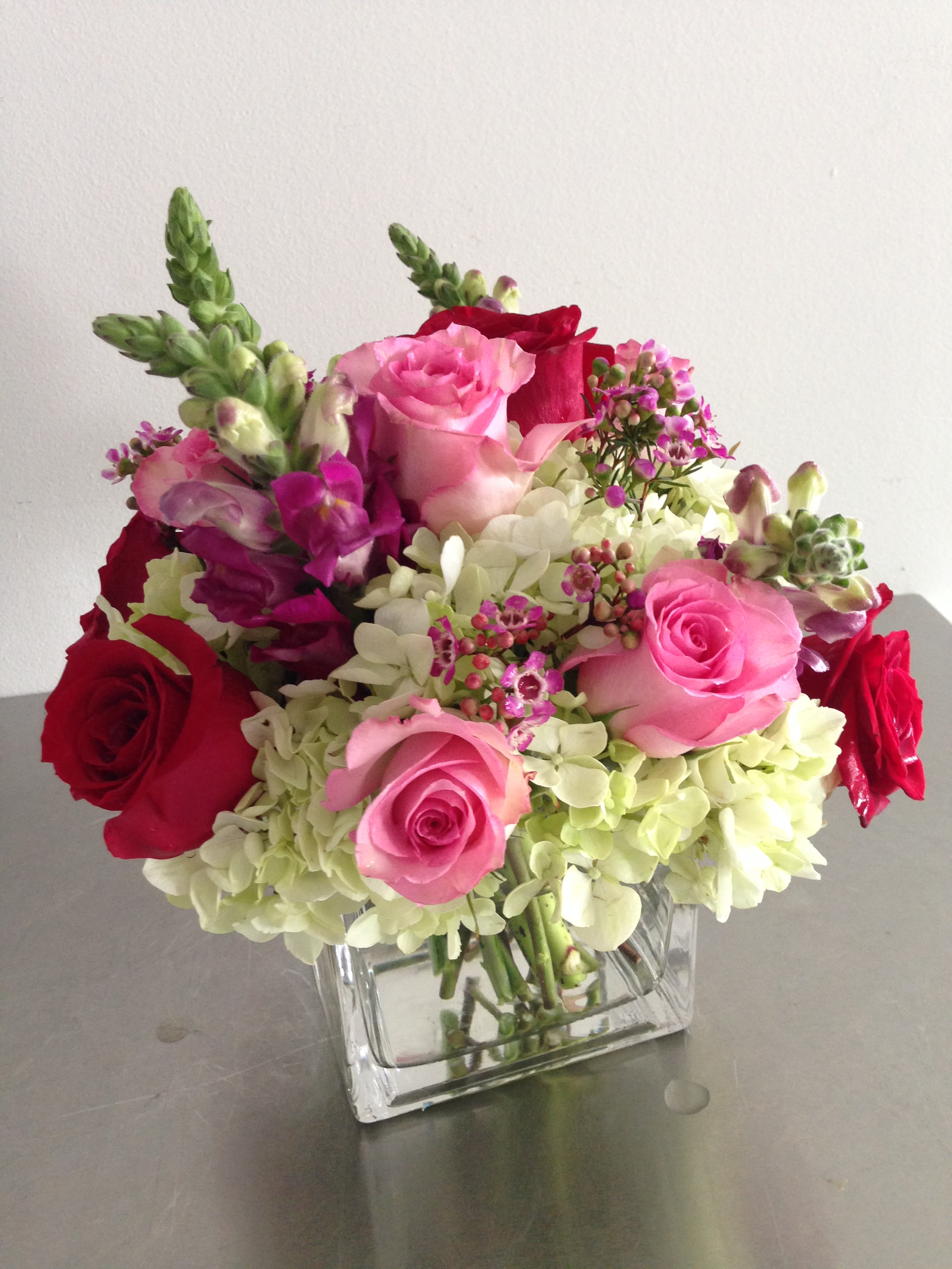Pink and red roses with white hydrangeas in a clear square vase