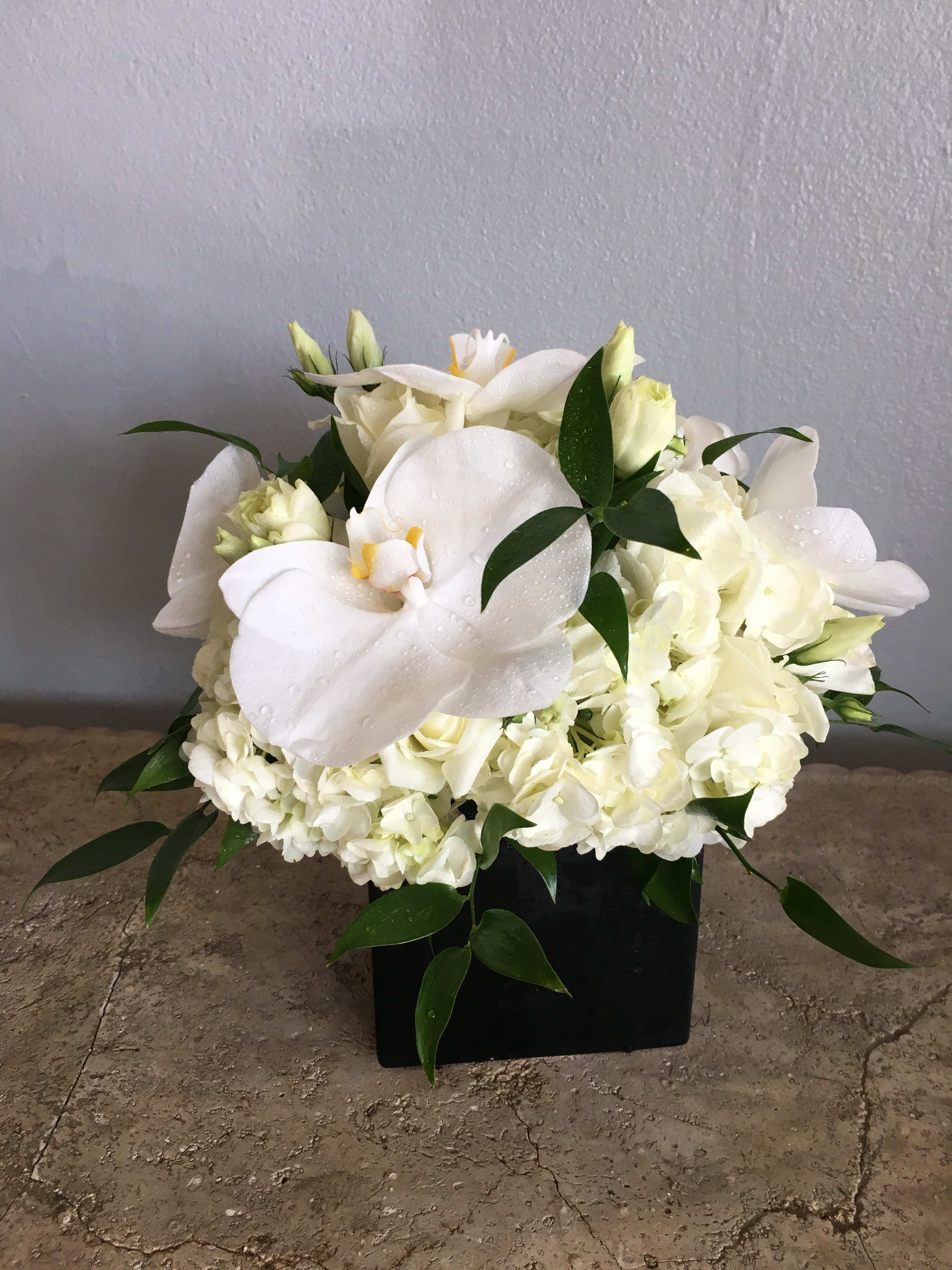 White floral arrangement with calla lilies and hydrangeas in a black container