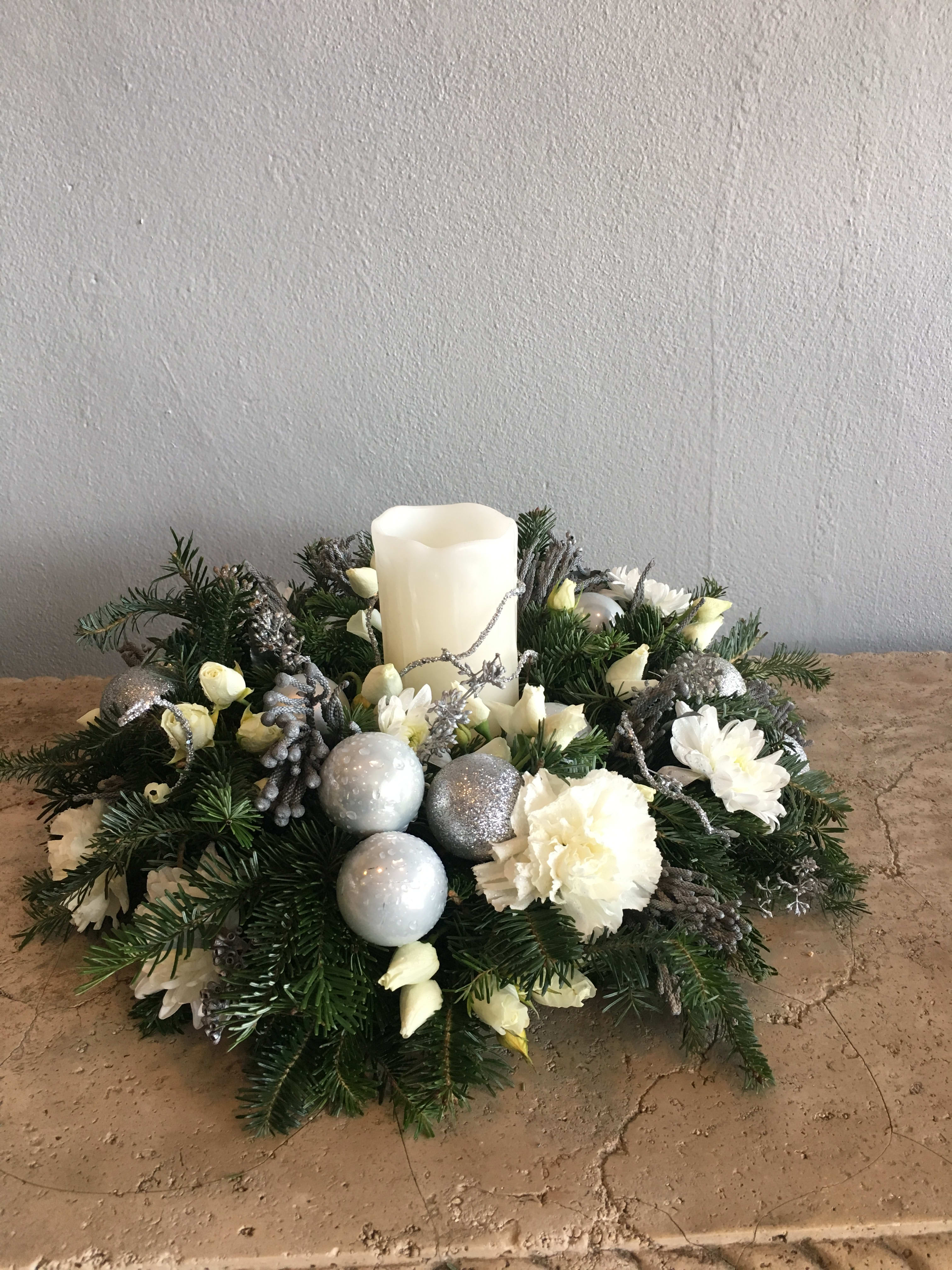 Holiday centerpiece with a white pillar candle, white flowers, and silver ornaments