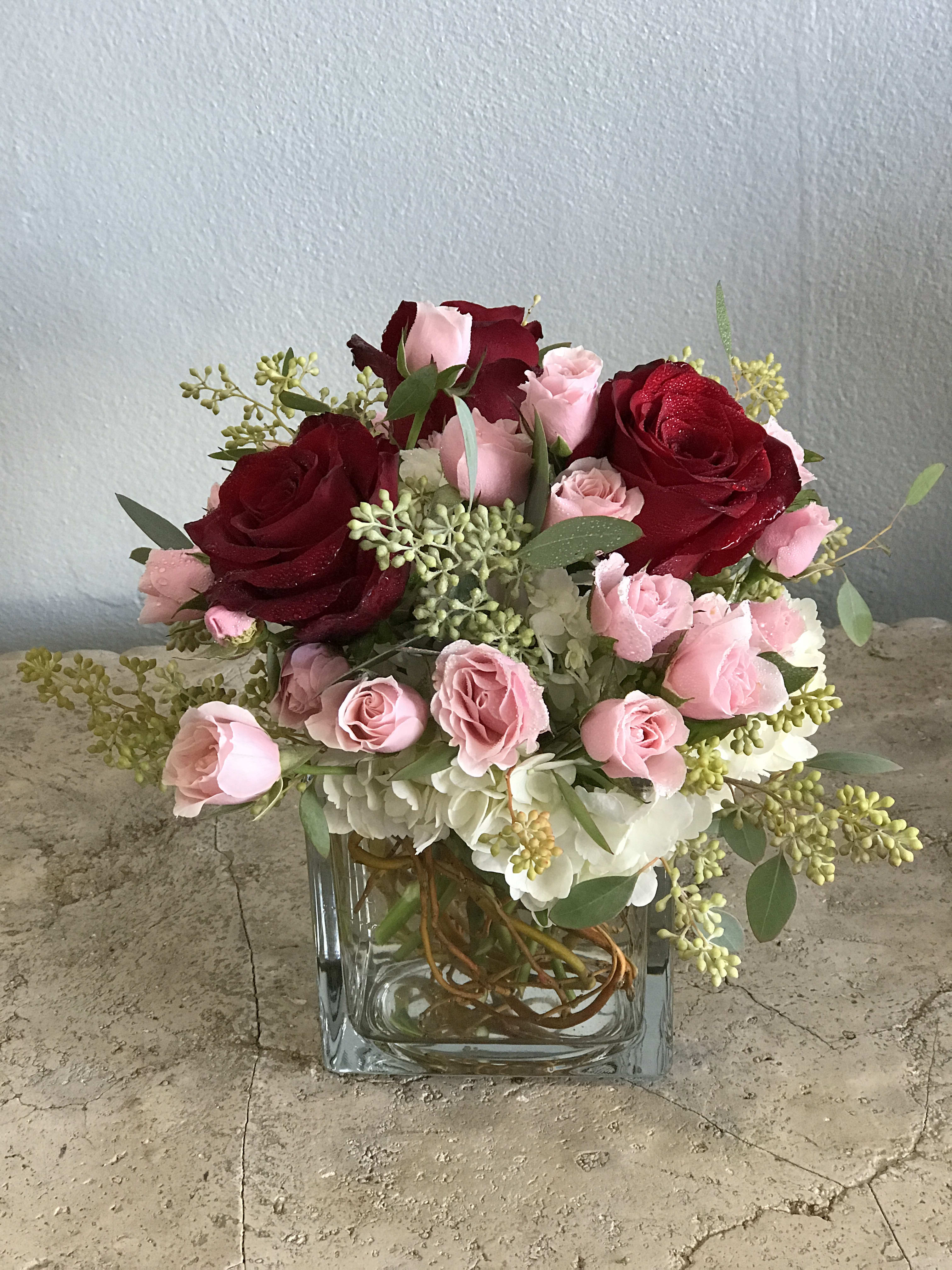 Pink and red roses arranged in a clear square vase