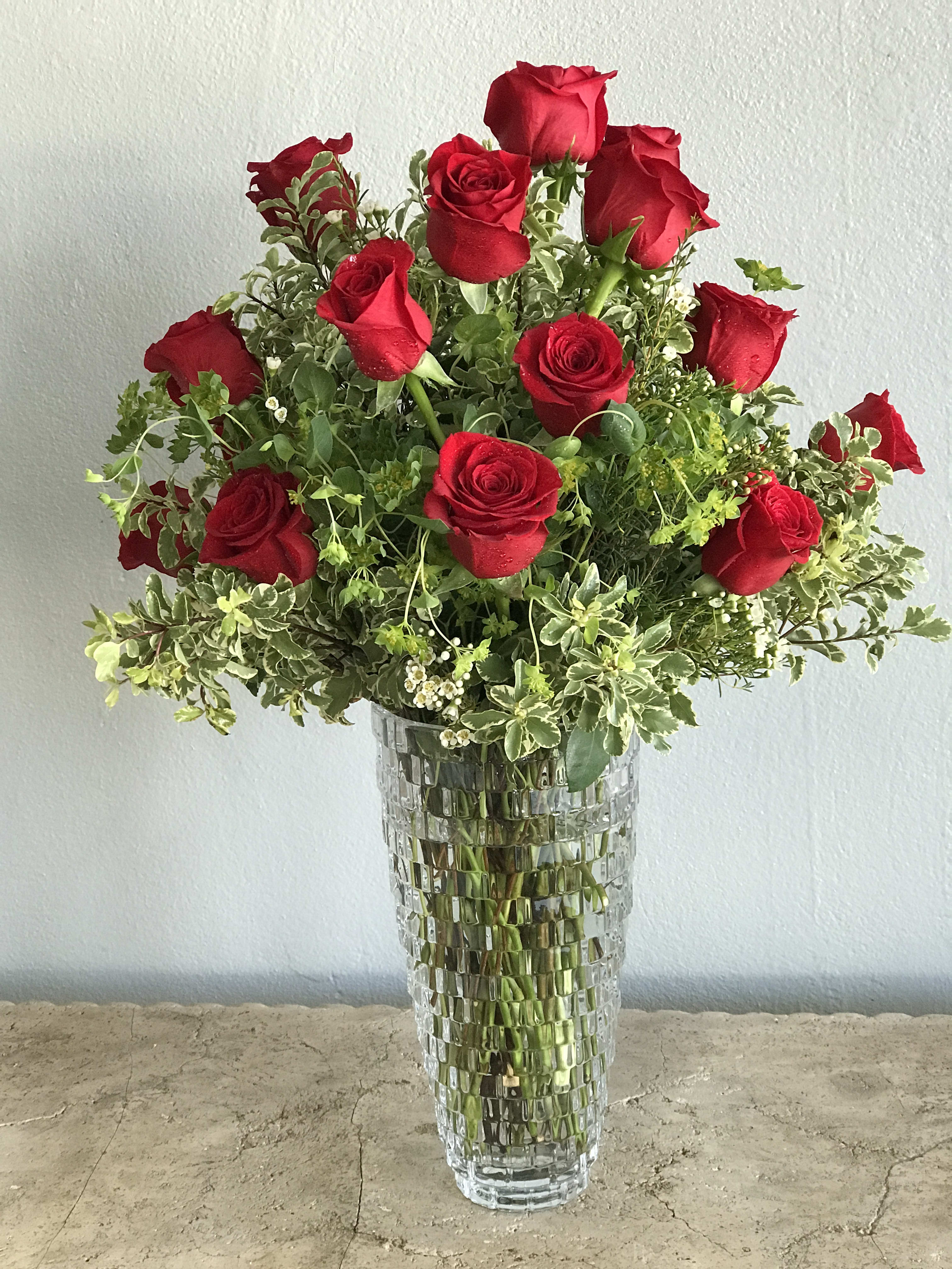 Red roses arranged in a tall glass vase with mixed greenery