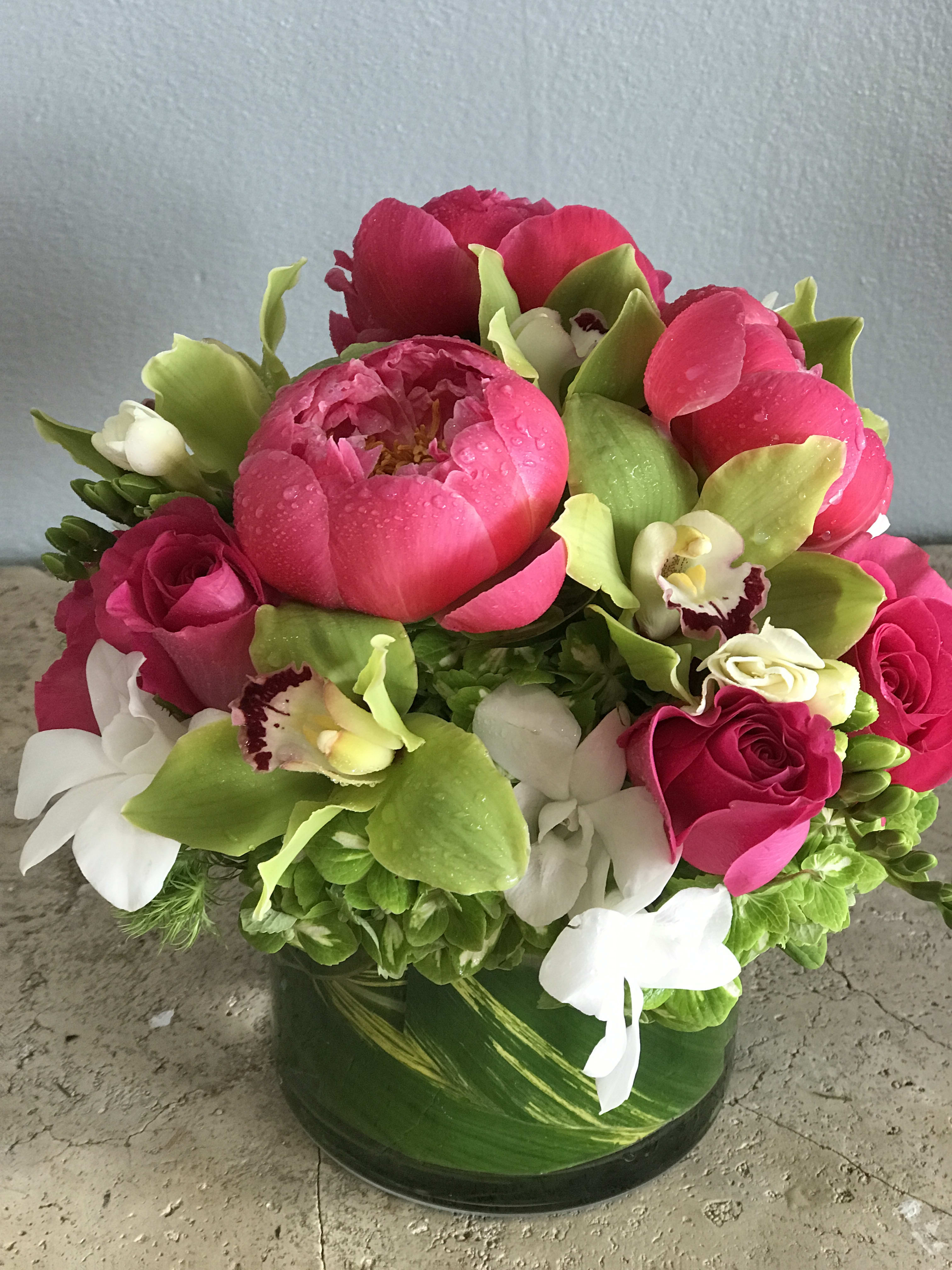 Pink peonies, roses, and white orchids in a green glass vase