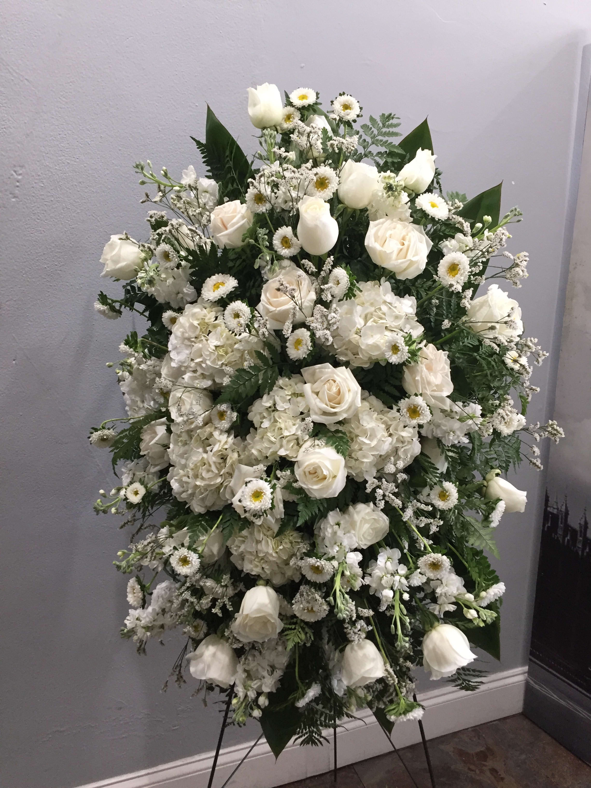 White floral standing spray with roses and daisies on an easel