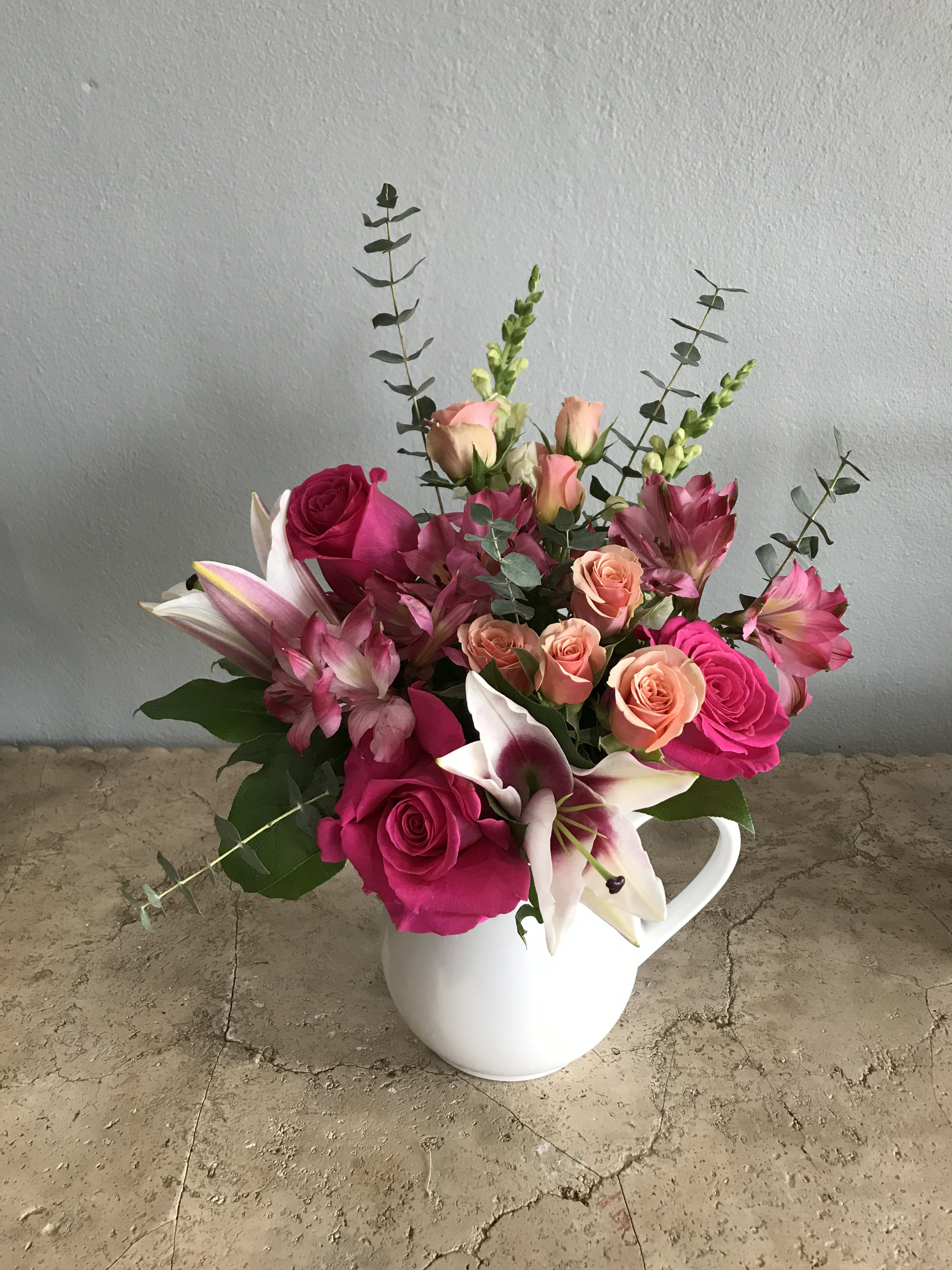 Pink and peach flowers arranged in a white pitcher vase
