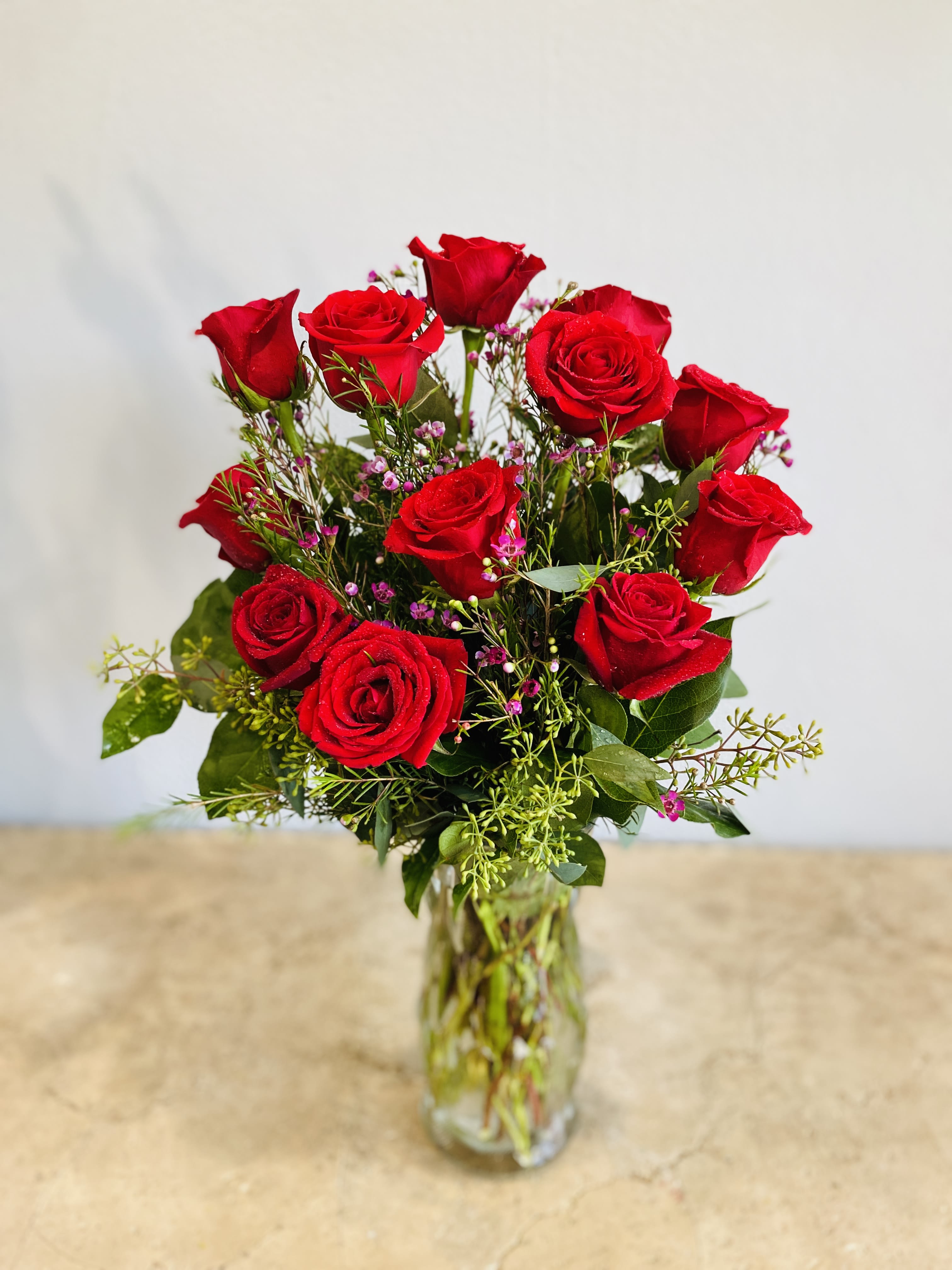 Red roses arranged in a clear glass vase with small pink filler flowers