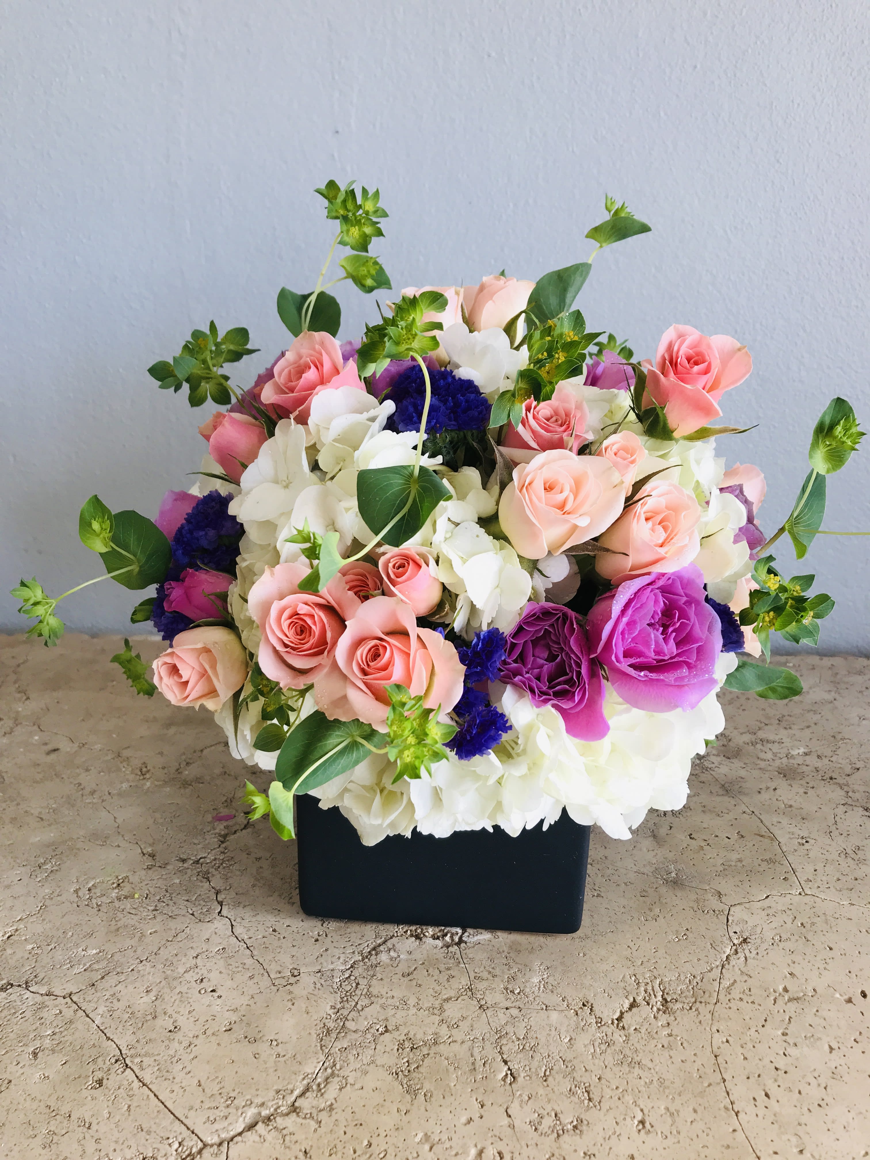 Mixed pink, white, and purple flower arrangement in a black box
